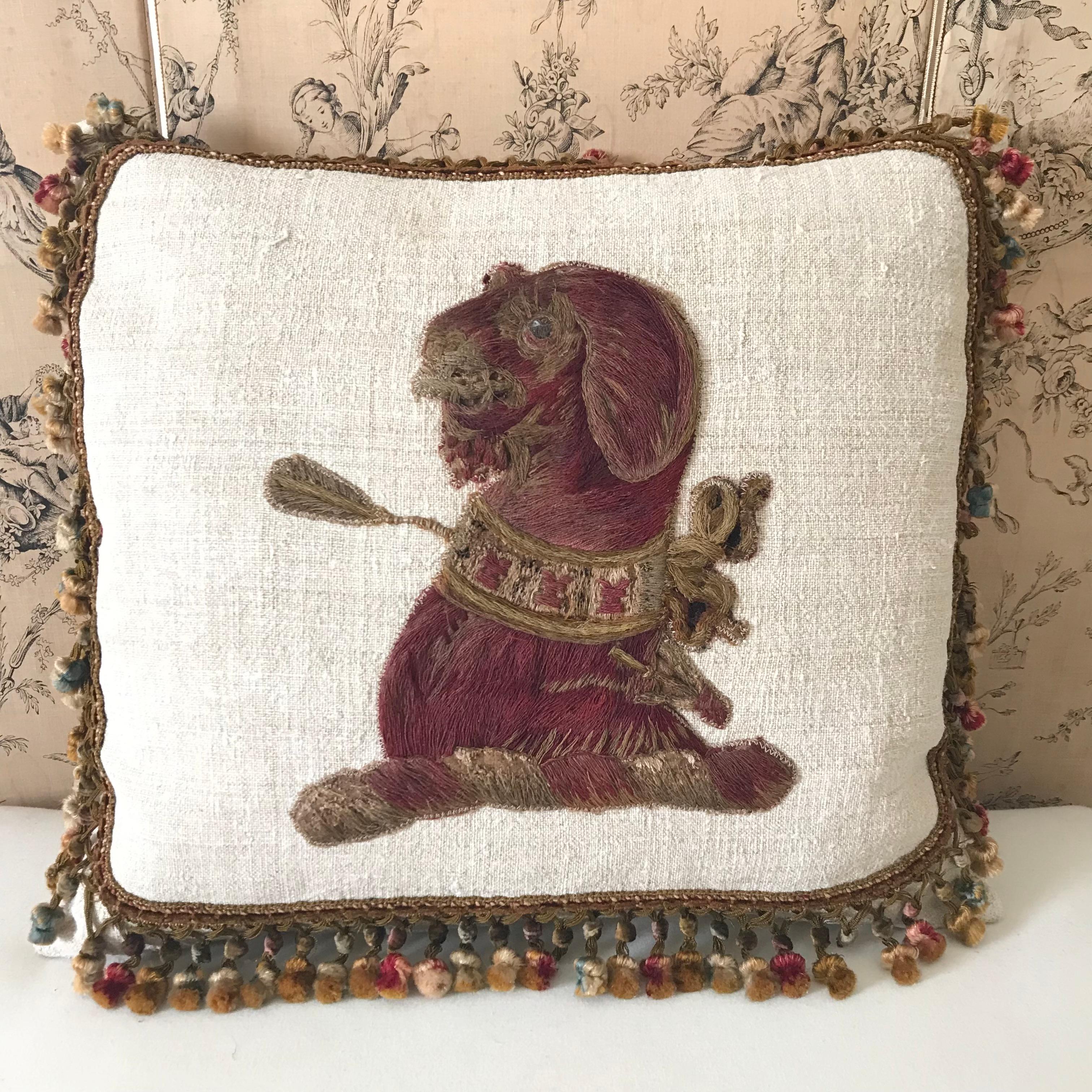 A beautiful cushion made from a rare and unusual 18th century hand embroidered stitched fragment of a regal looking dog placed onto antique linen with a wide early antique cut silk velvet passementerie to all edges in complimentary colours  - a