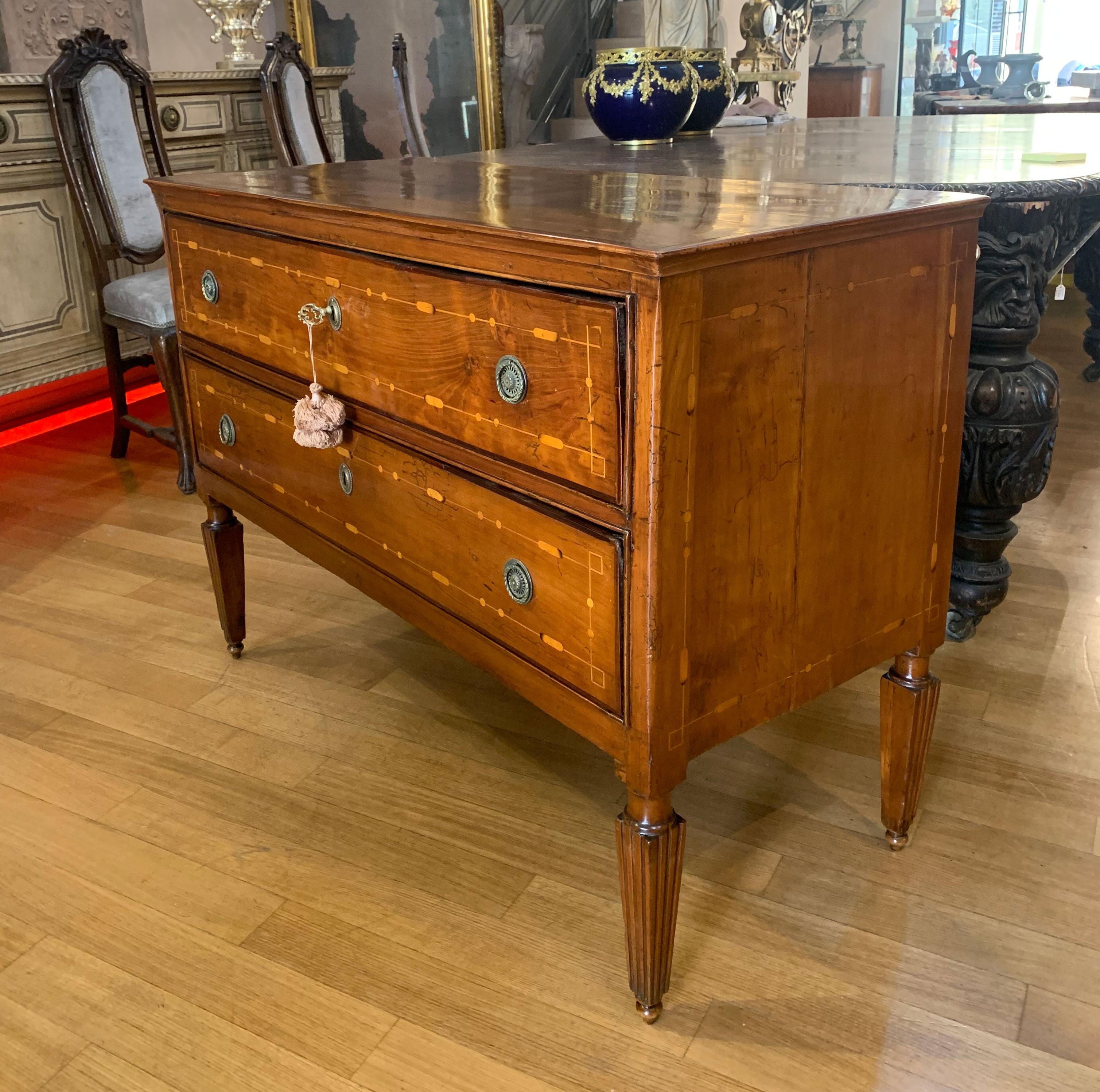 Elegant chest of drawers with neoclassical shapes with two drawers and truncated pyramidal feet in solid cherry, cherry veneer with very particular fillets with geometric motifs with the use of fruit woods. Typical Tuscan craftsmanship of the end of