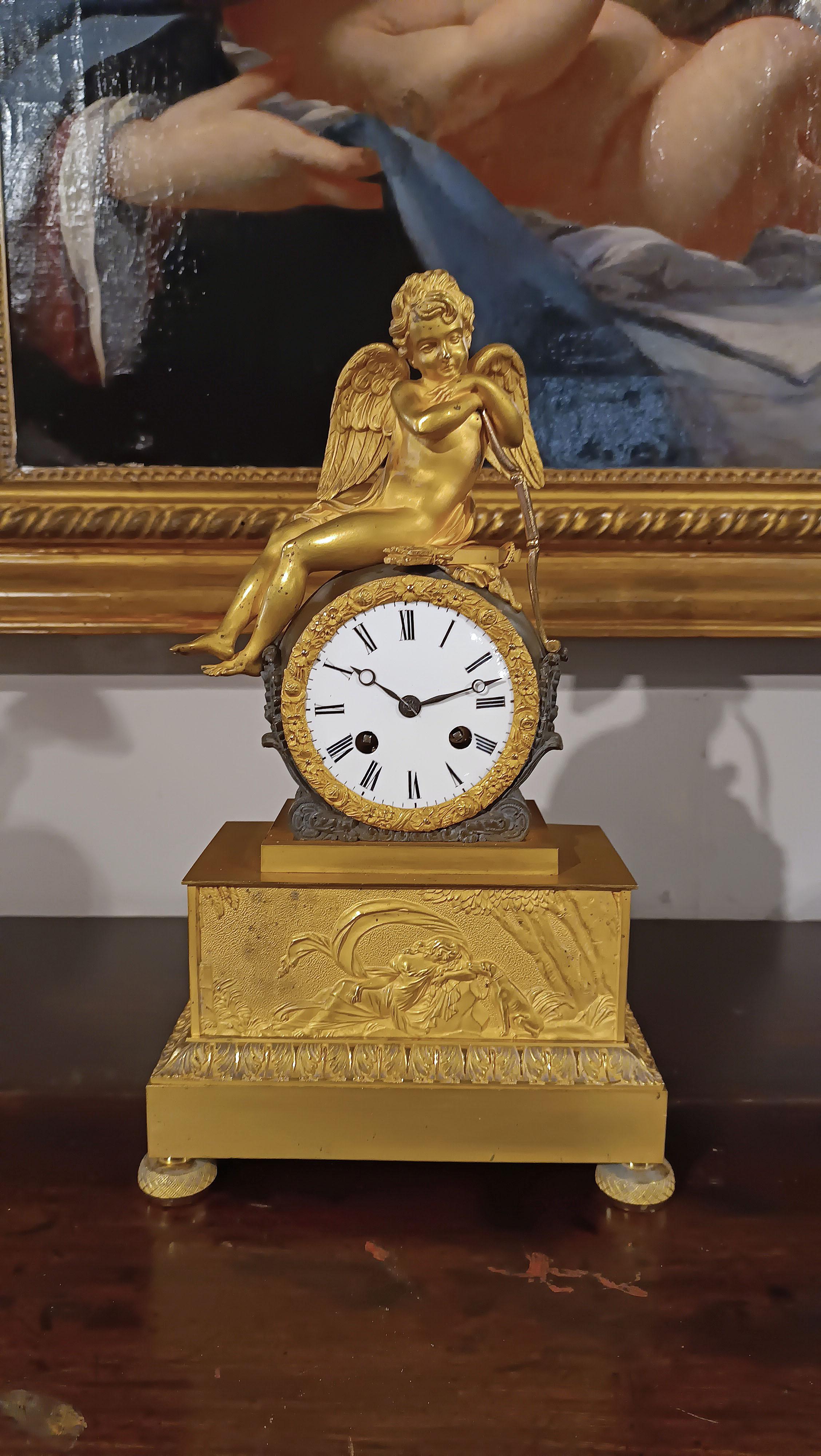 Beautiful and refined table clock in mercury-gilt bronze, with original gilding. The decoration presents the allegory of love, with Cupid sitting and leaning on the arch, while on the base his mother Venus is depicted lying in the shade next to a