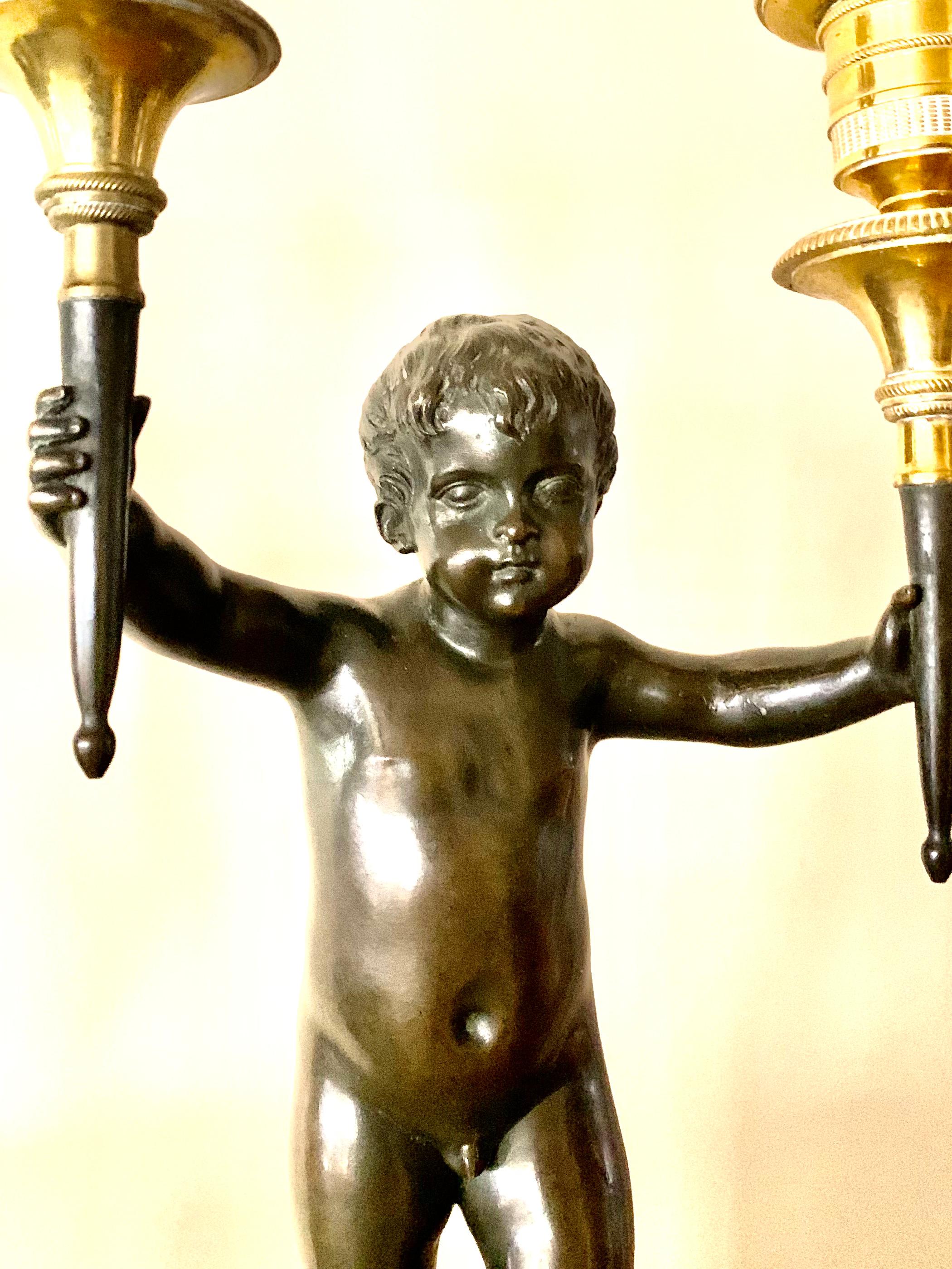 Fine pair of Dore and patinated bronze figural putti 18th century two light candelabra on original Saint Anne marble plinths. Each individually modelled as a classical youth holding a pair of torch shaped dore bronze candelabra on rectangular dore