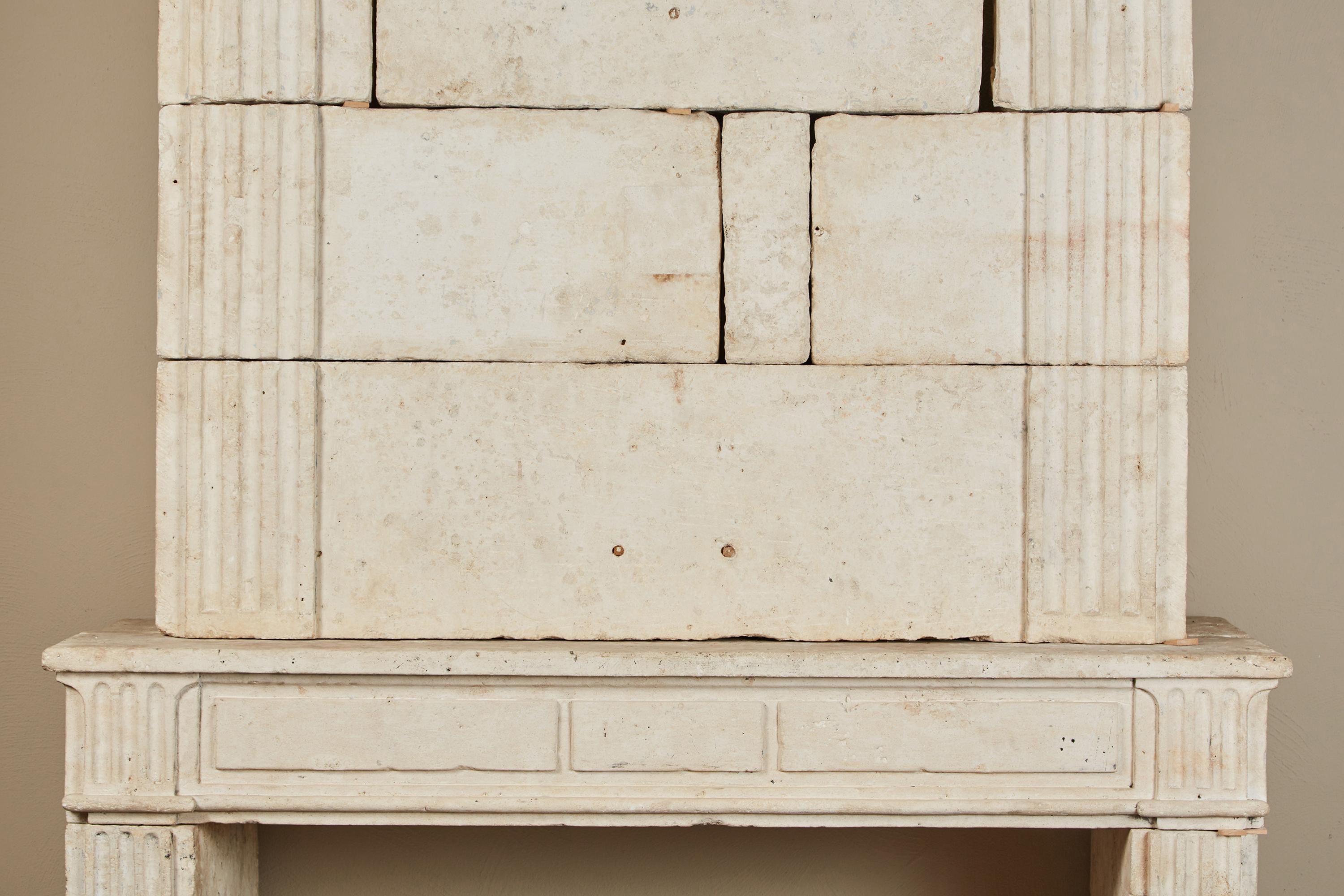 Eine Kamineinfassung aus französischem Kalkstein aus dem 18. Jahrhundert im neoklassischen Stil. Der obere Teil ist von beeindruckender Größe, mit einem breiten, profilierten Gesims und breiten, kannelierten Pilastern. Der untere Teil ist mit