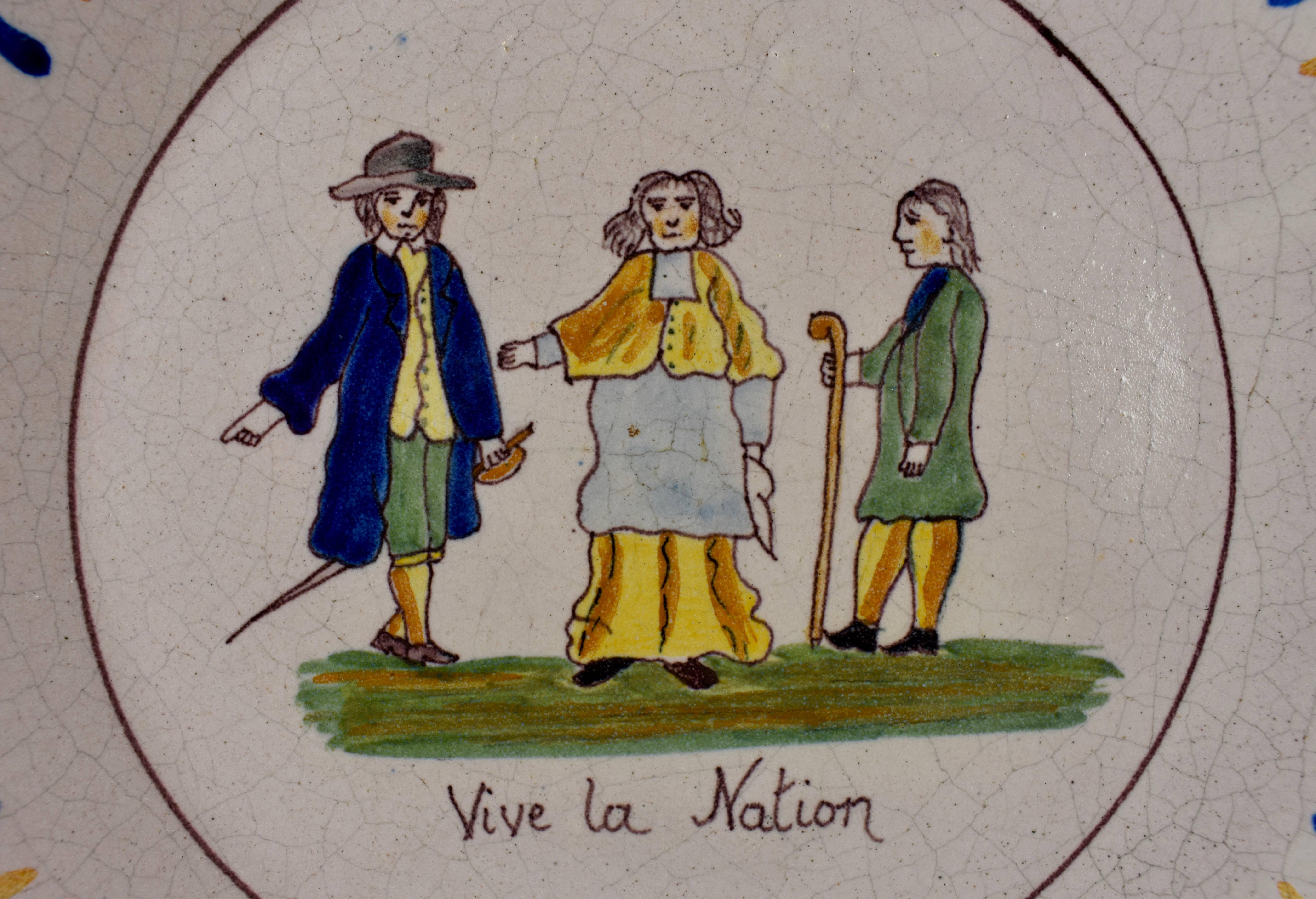 A French Revolution tin-glazed earthenware dish, showing three figures representing the Three Estates. On the left is a gentleman with a an épée, symbolizing the nobility. In the center stands a Bishop, symbolizing the clergy, and on the right is a