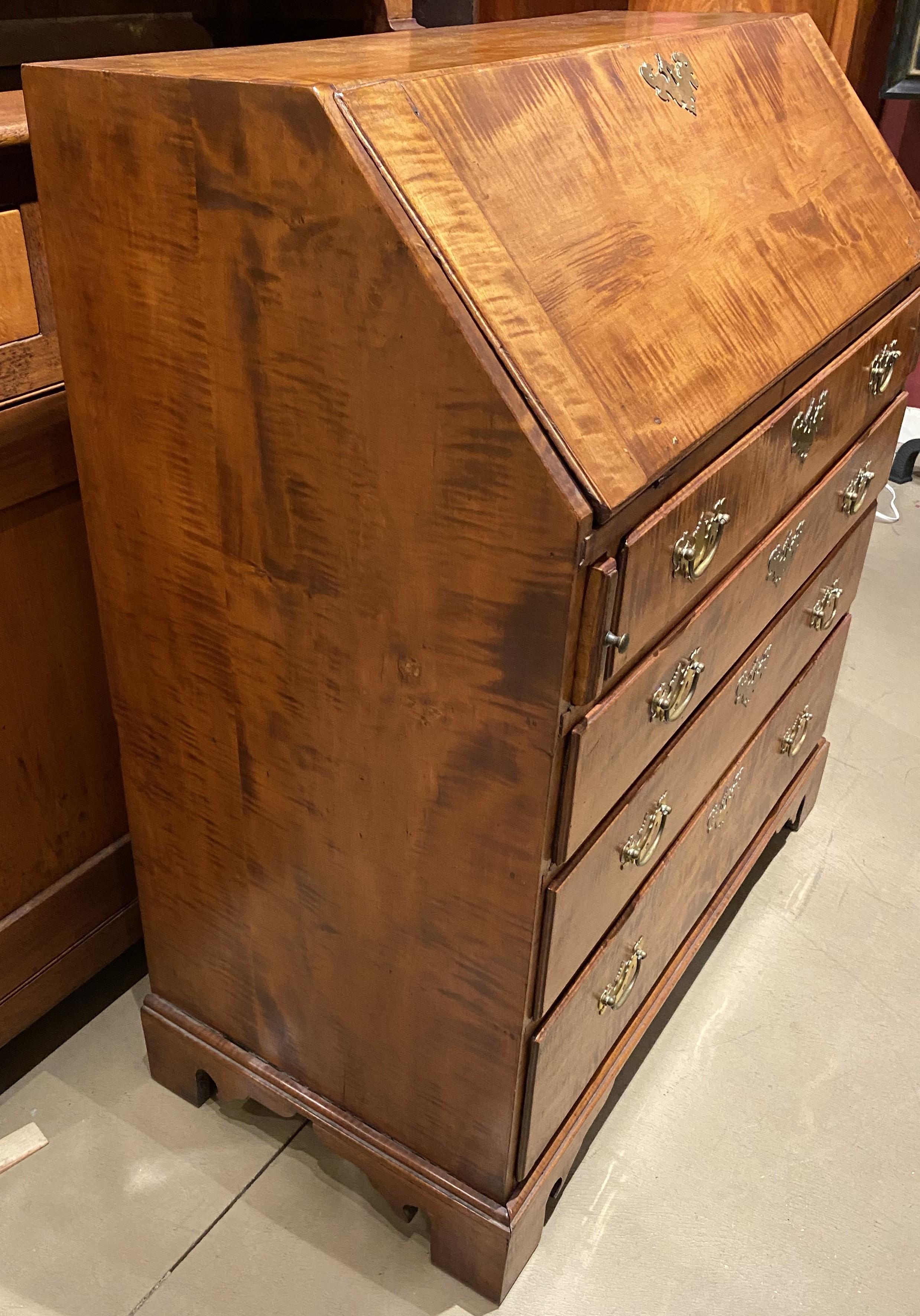 A fine slant front desk in tiger maple with compartmentalized interior with eight open cubbies and three fitted drawers, over four long dovetailed drawers, each with replaced batwing brasses, all supported by nicely carved bracket base.  Dates to