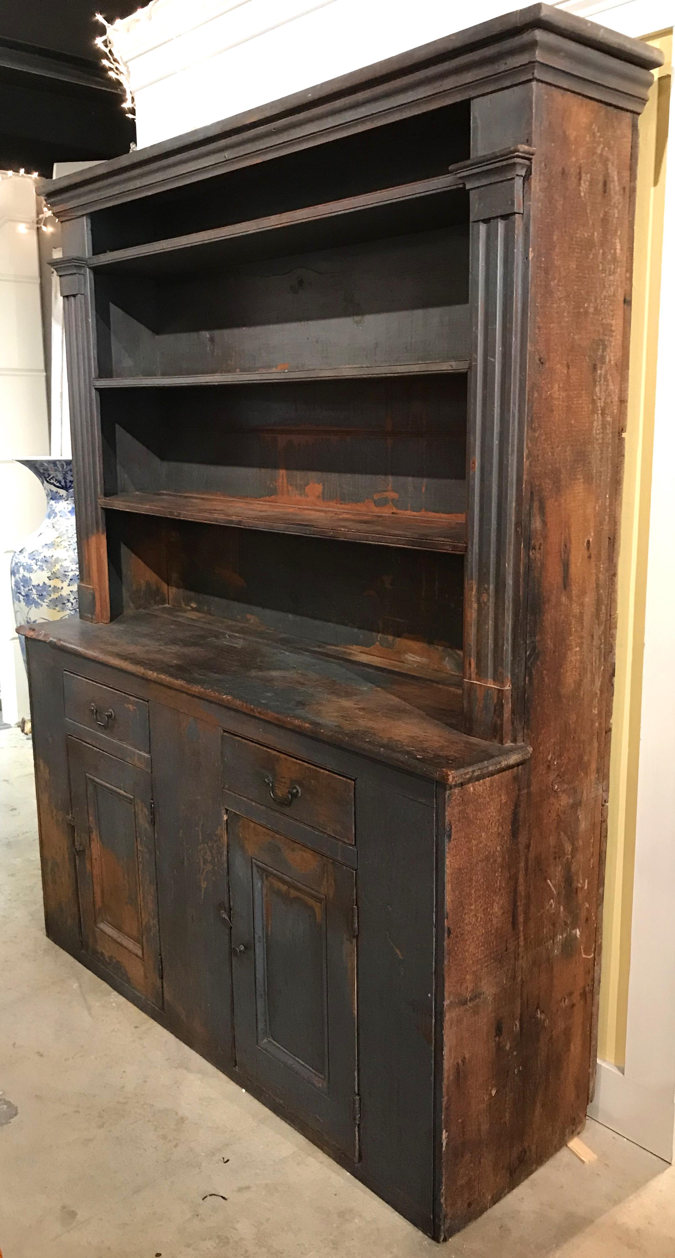 A fine Primitive American open top pewter cupboard in old blue paint, with molded cornice surmounting a three shelf open top with plate rails, flanked by reeded pilasters, over two fitted drawers and two paneled doors opening to a single shelf with