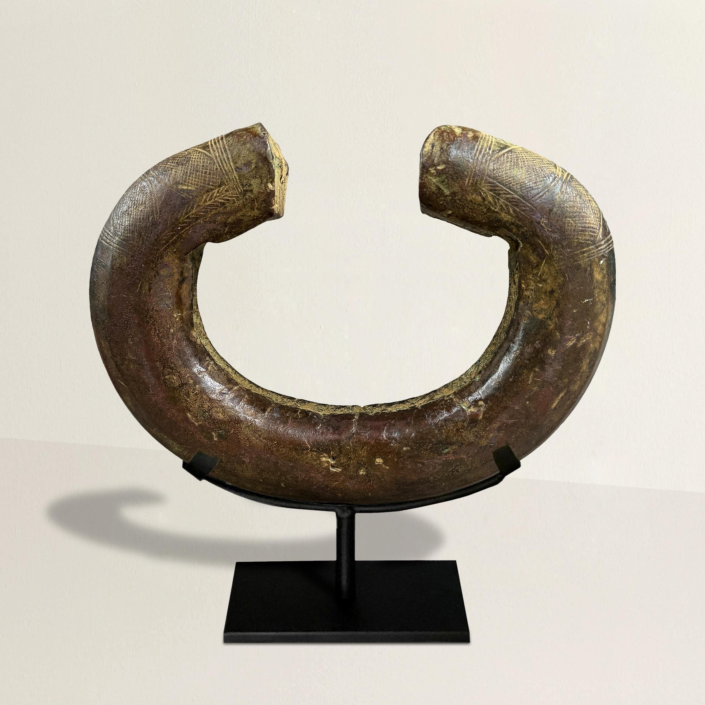 Esta rara manilla de moneda de bronce Ngelima del siglo XVIII es un artefacto asombroso, con un impresionante peso de 9 kilos de bronce macizo. Adornada con intrincados dibujos lineales incisos en sus extremos, esta pieza es a la vez un artículo