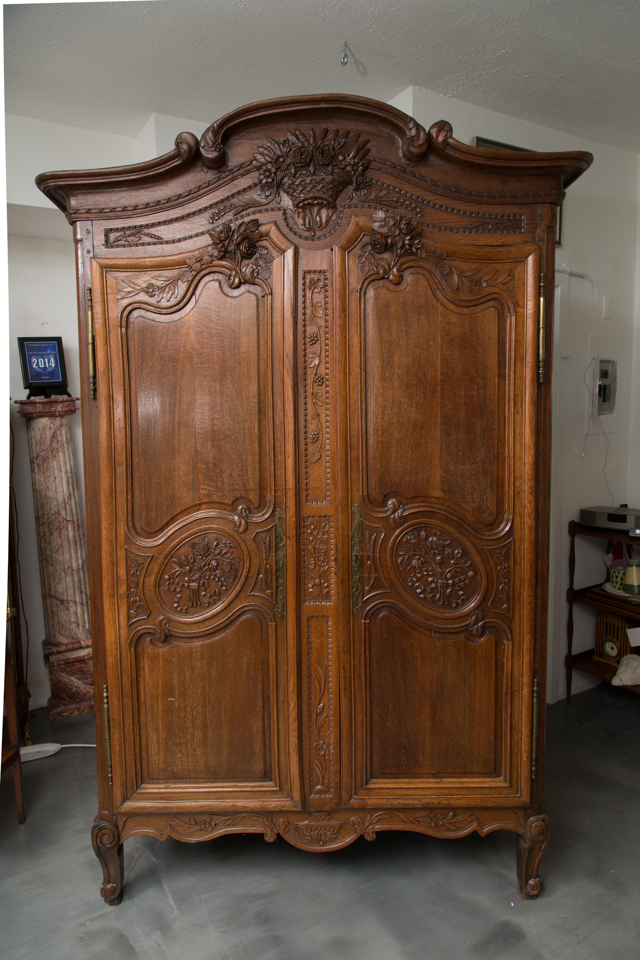 This is a stunning example of a Louis XV walnut Normandy armoire. A cornice tops a with bold moulding arching in the centre over a traditional carved basket of flowers above two paneled doors accented with floral spray and supported by short