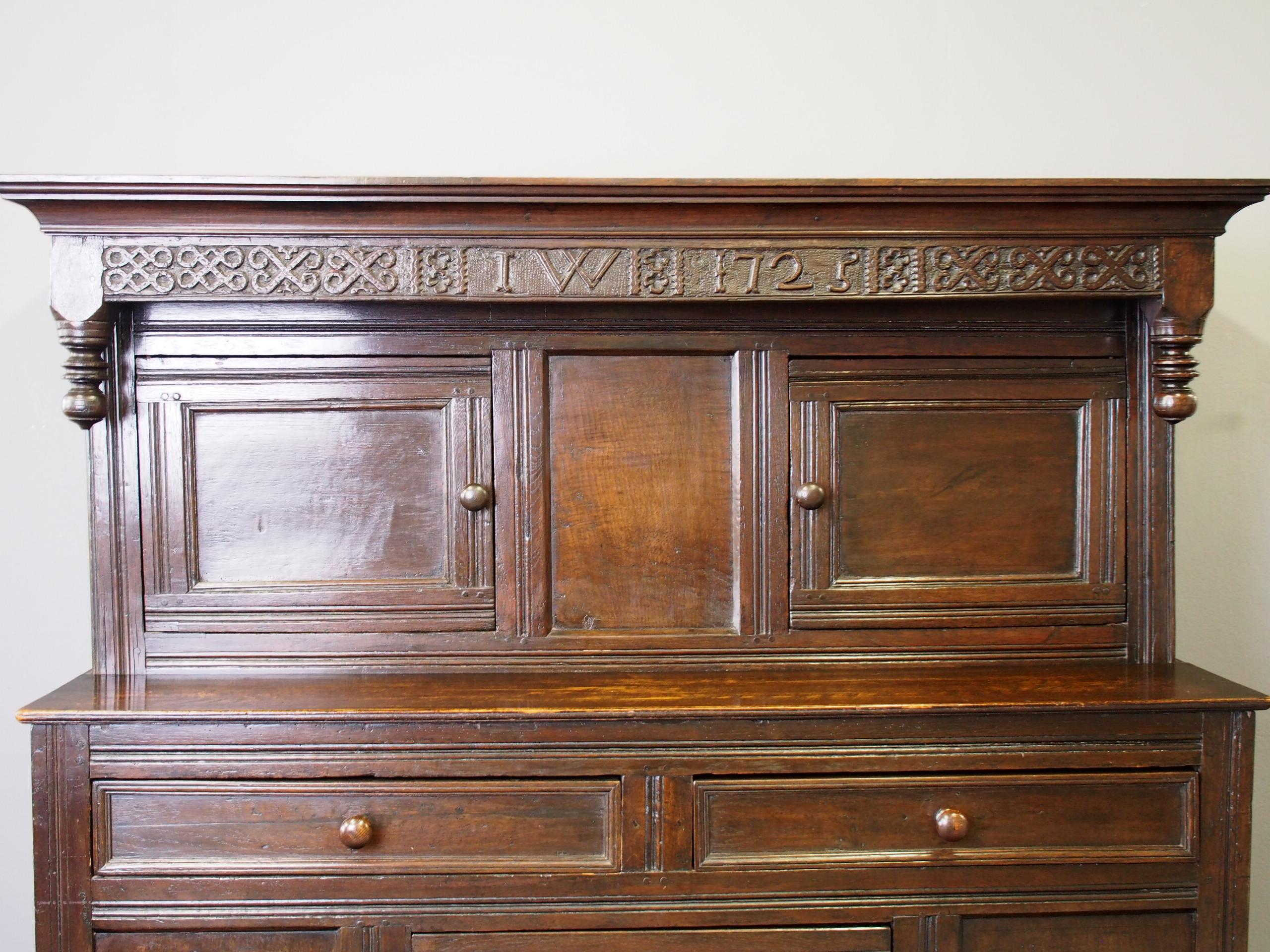 Dated 1725, Northern English carved oak cupboard. Initialled and dated, with moulded corners, carved finials and panelled doors opening to an uninterrupted interior. With blacksmith-made steel hinges, and the bottom section has 2 narrow drawers. The