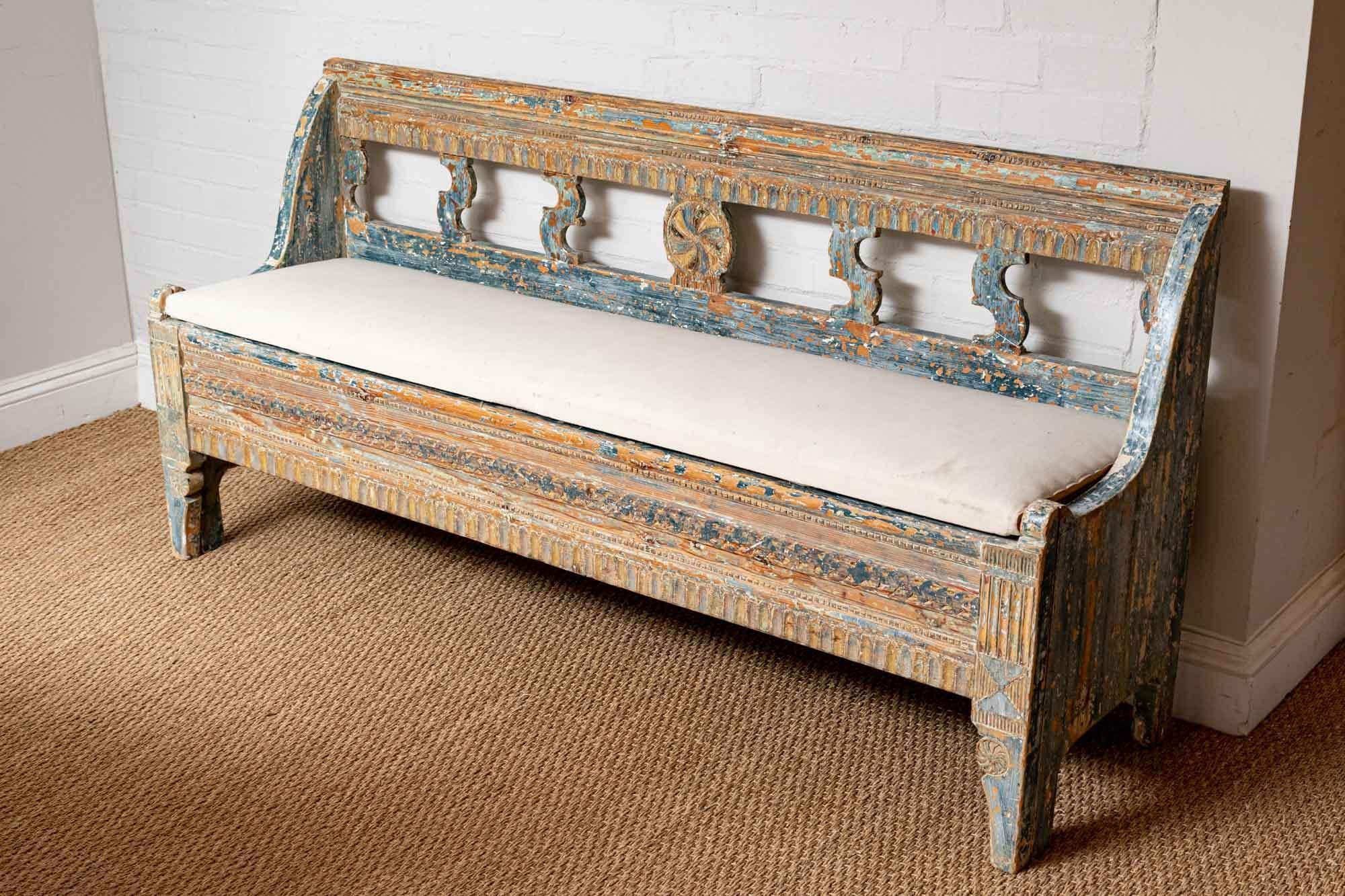 Late 18th century, highly decorative, solid Norwegian bench retaining most of its original paint in different shades of blue. The bench is hand carved to the front with decorative scroll detail at the back. It has a simply covered upholstered drop