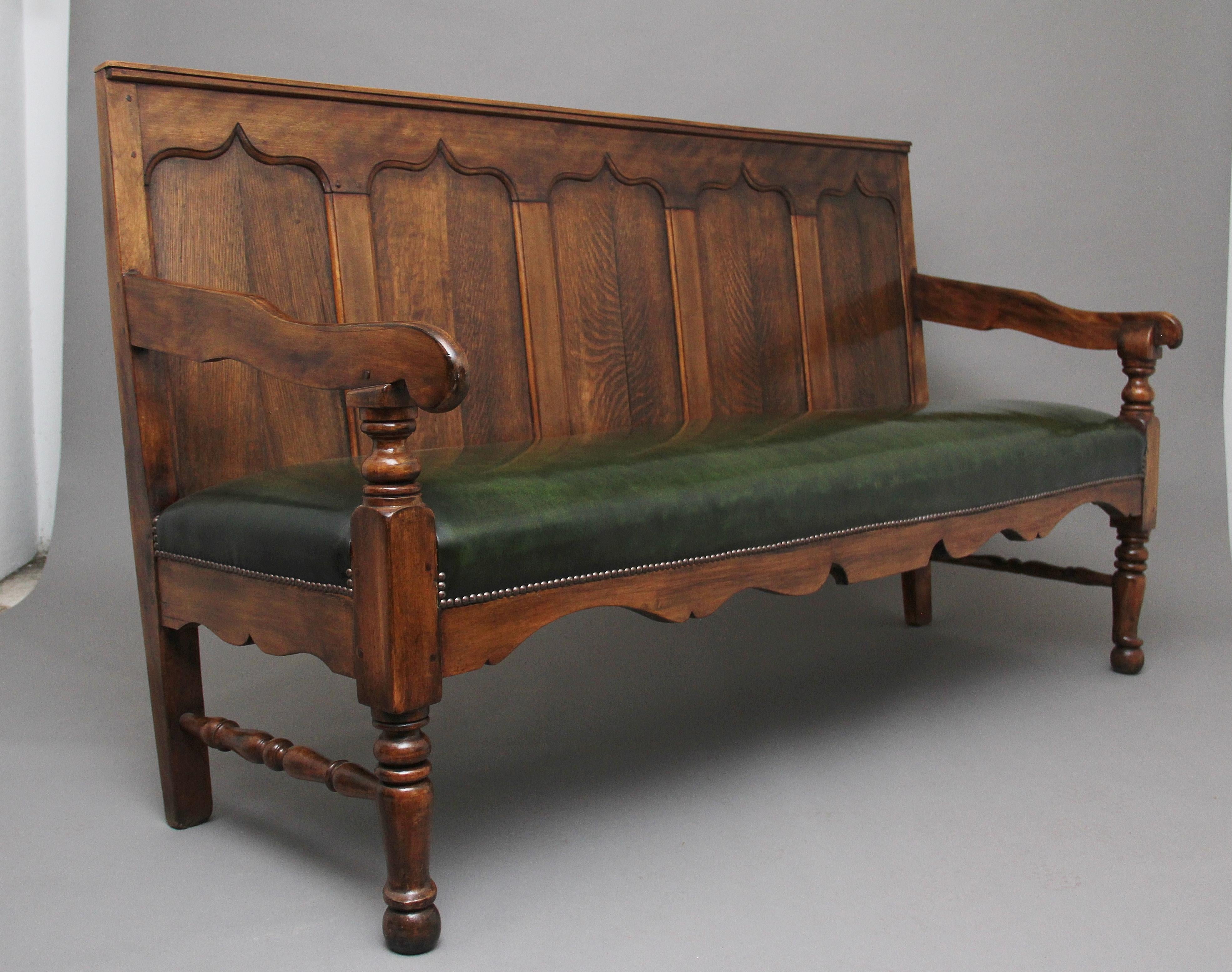 18th century oak and fruitwood bench or settle, the high back with five fielded oak panels flanked by down swept arms on turned supports enclosing the recently upholstered green leather seat with brass stud decoration, nice shaped apron below,