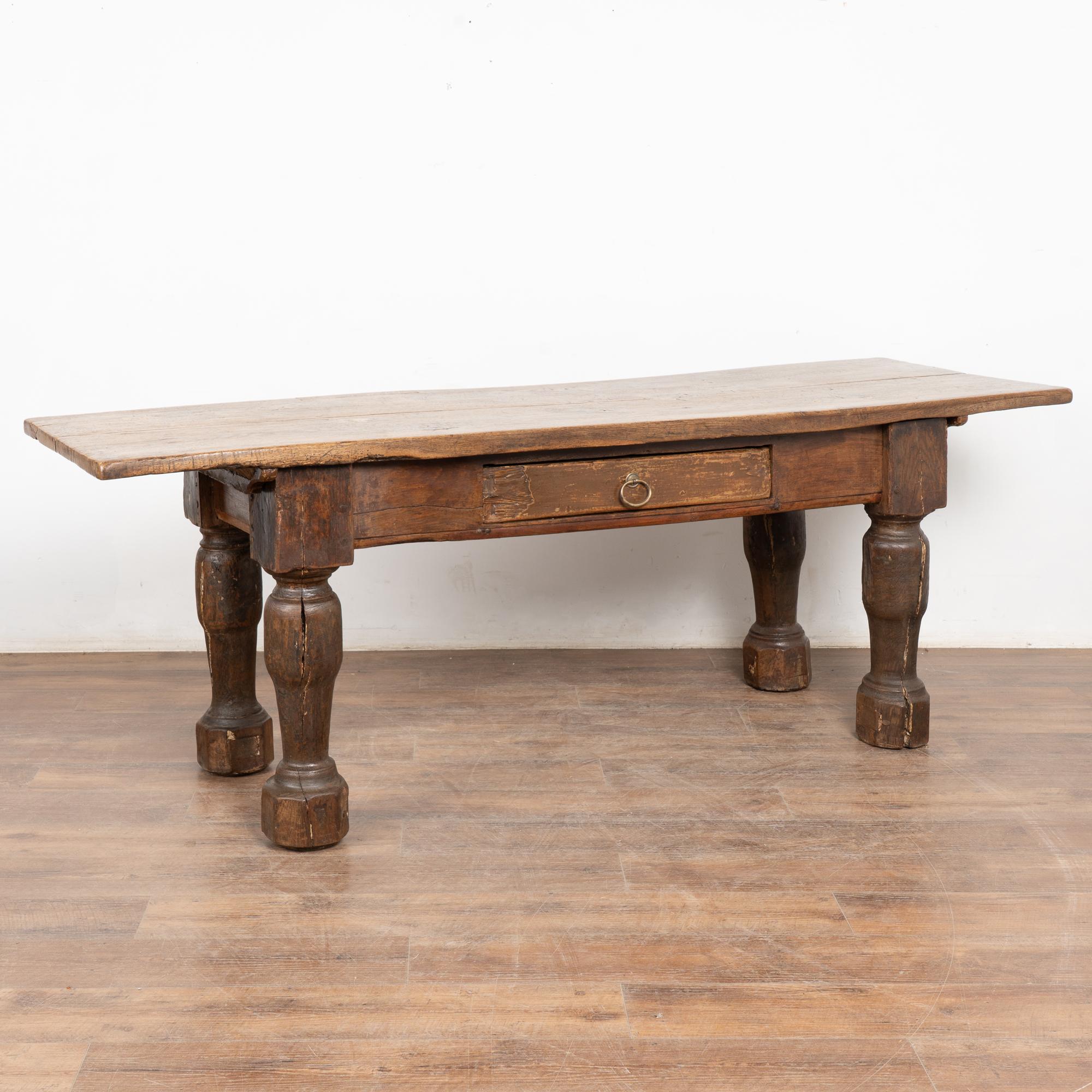 This handsome baroque style oak library table with one drawer has heavily turned legs and is over 7' long.
Distress from generations of use is seen throughout this table including old cracks along legs, feet and table top. Old repairs are seen in
