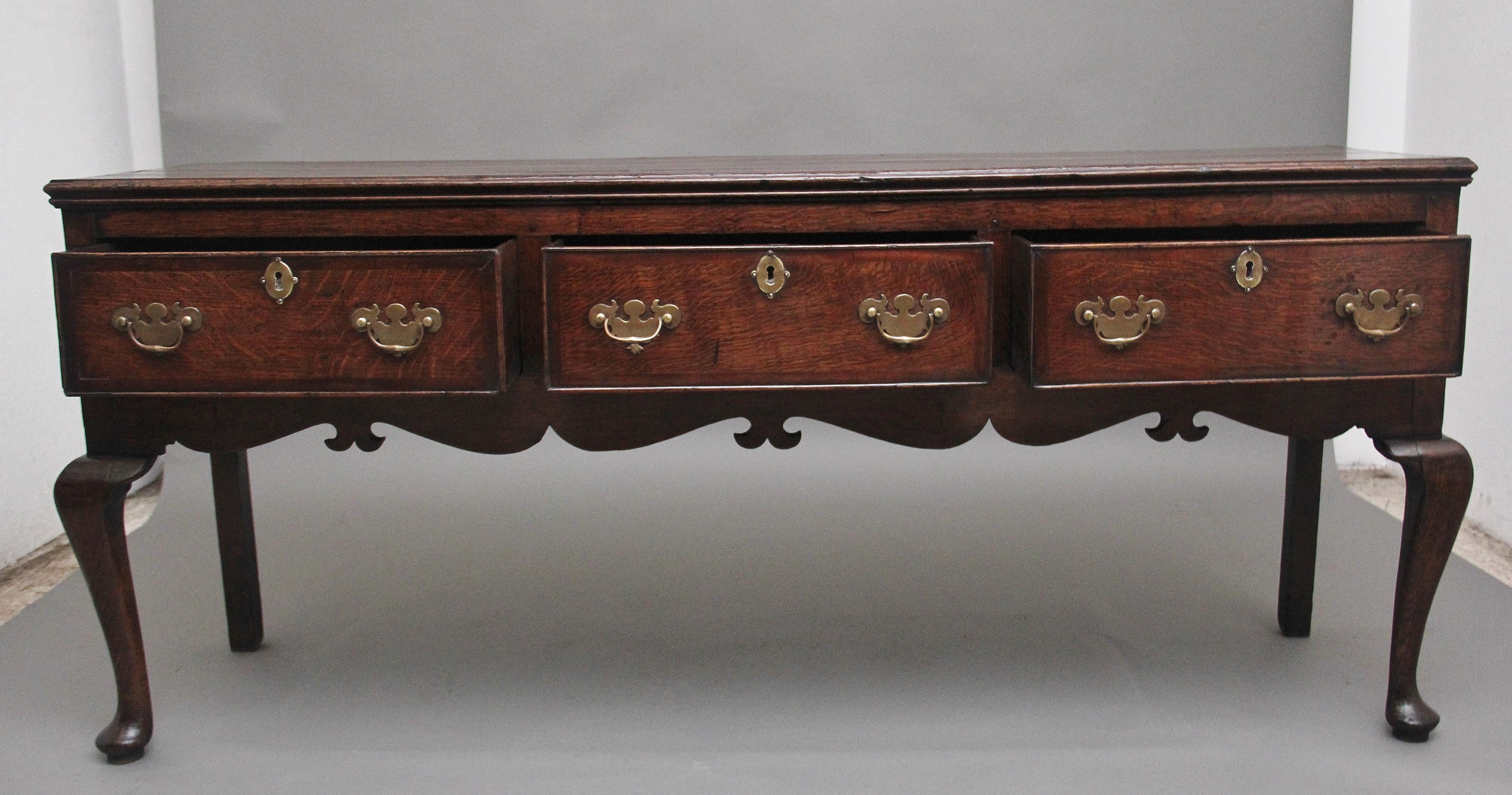 A superb quality 18th Century oak dresser base, having a lovely figured and moulded edge top above three deep drawers with the original brass plate handles and escutcheons, lovely figuration on the drawer fronts, decorative shaped frieze below and