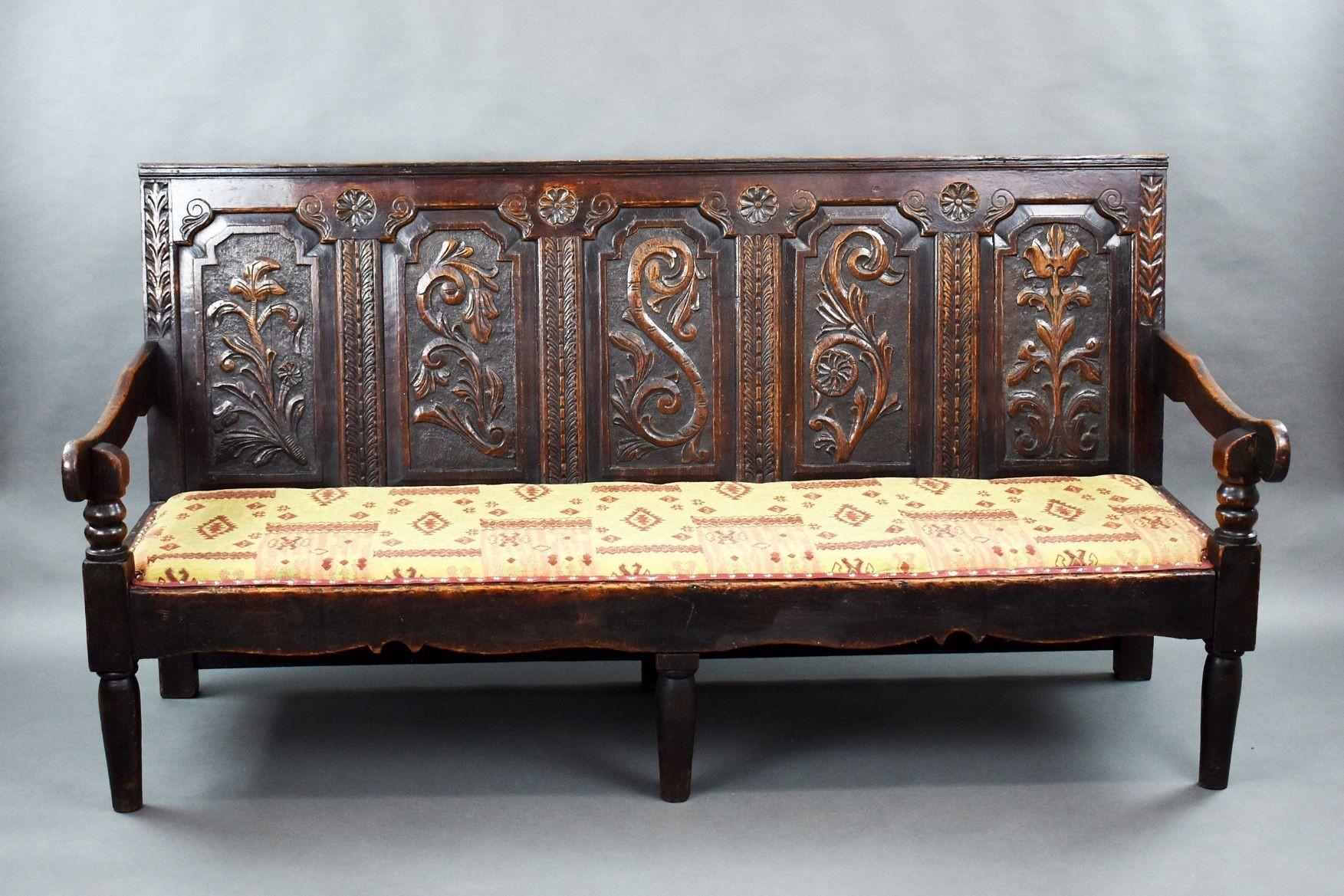 18th century Carved Oak settle with upholstered seat with profusely carved back standing on turned legs.