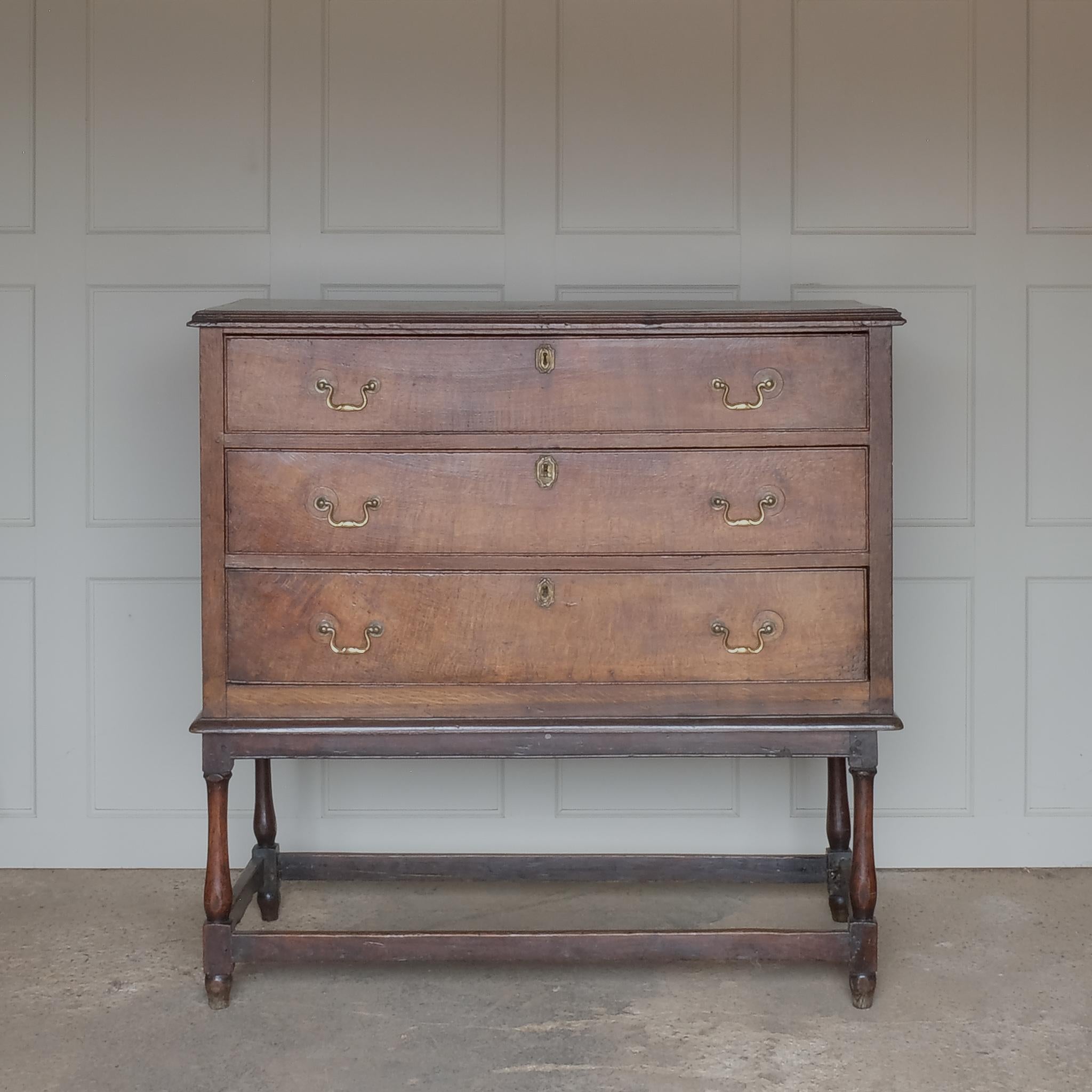 An oak chest on legs, 18th century, comprising three long drawers with brass drop handles and platework on turned legs with rectangular stretchers at the base. In very good condition throughout, a wonderful rich patina. 