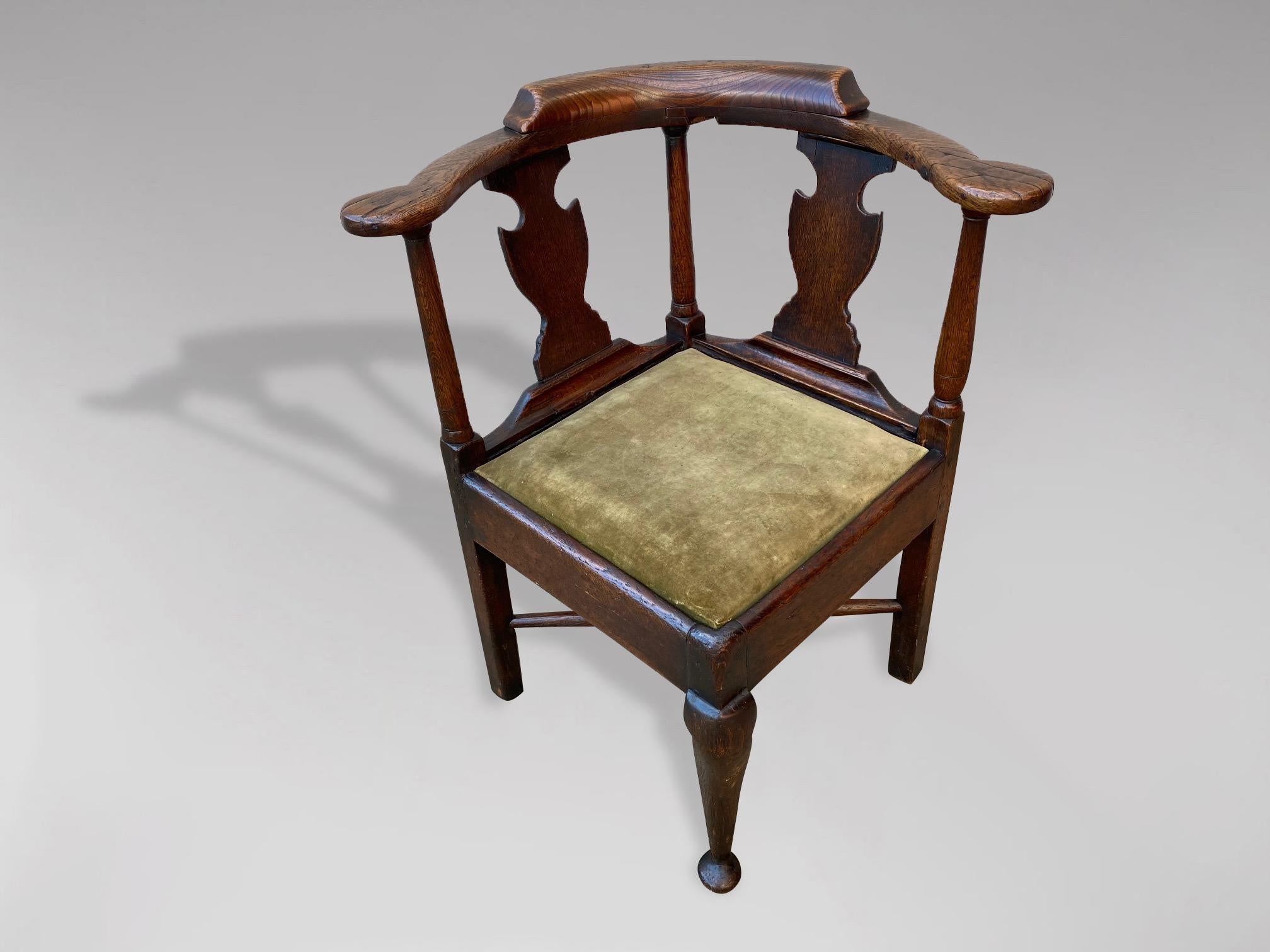 An 18th century, Georgian period oak corner chair. The shaped top rail supported by baluster turned supports and back splats, with green velvet upholstered drop in seat raised on three squared legs and a centre cabriole leg with pad feet all