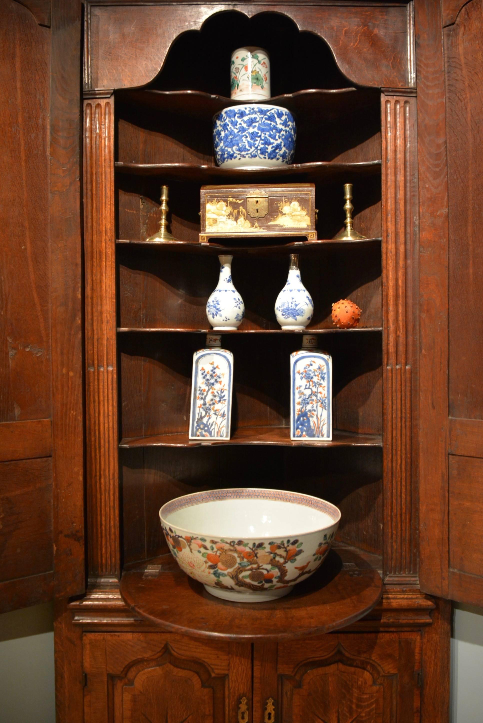 A George II oak double height standing corner cupboard. The ogee arch topped doors crossbanded and inlaid with large starbursts, the upper doors opening to reveal an architectural interior with shaped shells and it's original demilune serving flap,