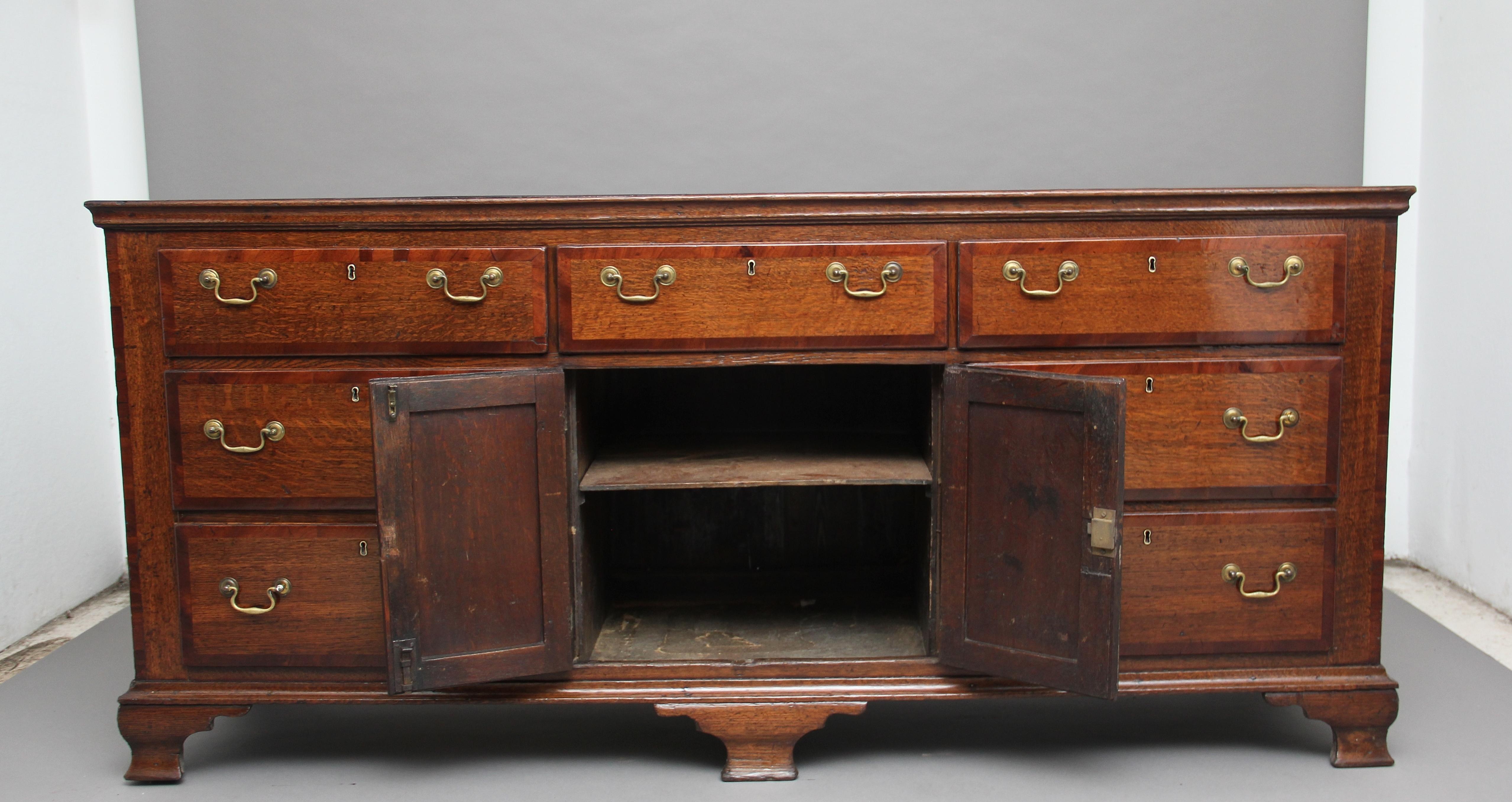 A large 18th century Cheshire oak dresser base, the top crossbanded in mahogany above a selection of seven crossbanded drawers, one drawer at the top centre flanked either side by three graduated drawers, the drawers having brass swan neck handles
