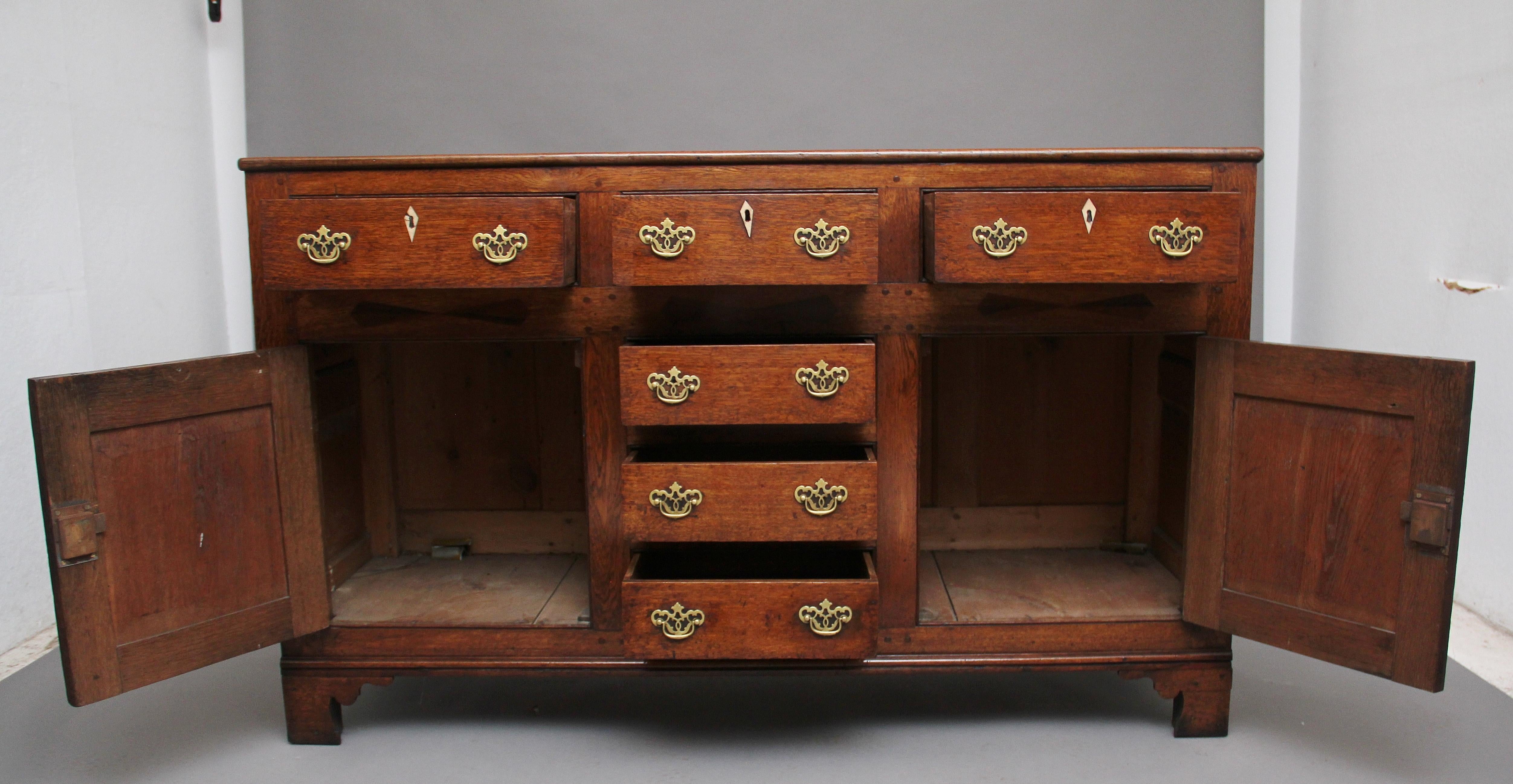 18th century oak dresser base, having a wonderfully figured top above a selection of three over three drawers with brass fret handles, the drawers in the centre flanked either side with cupboard doors with fielded arch panels, opening to reveal a