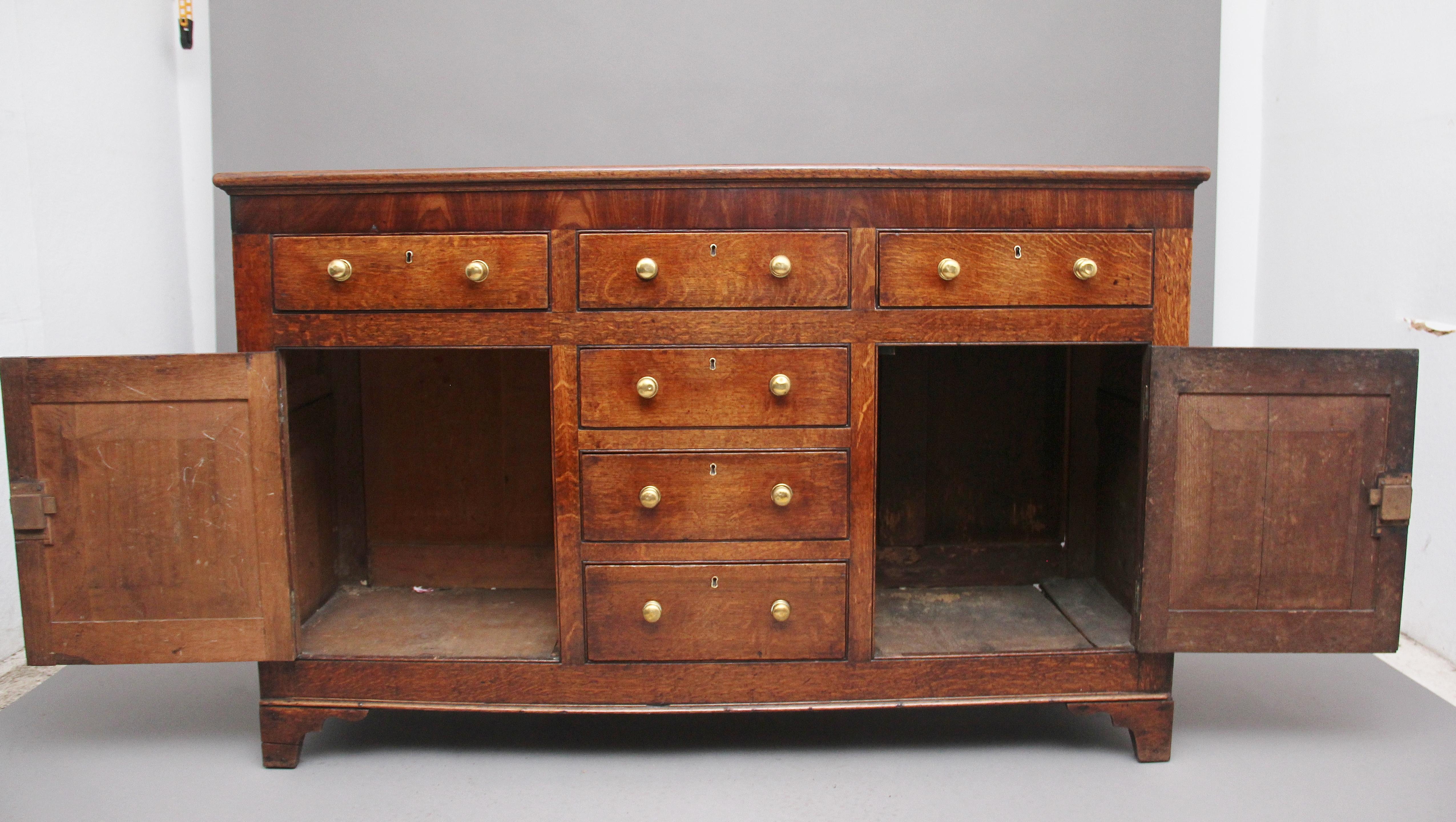 18th century oak dresser base, having a wonderfully figured top above a selection of three over three graduated drawers with original brass turned knob handles, the drawers in the centre flanked either side with hinged cupboard doors with moulded