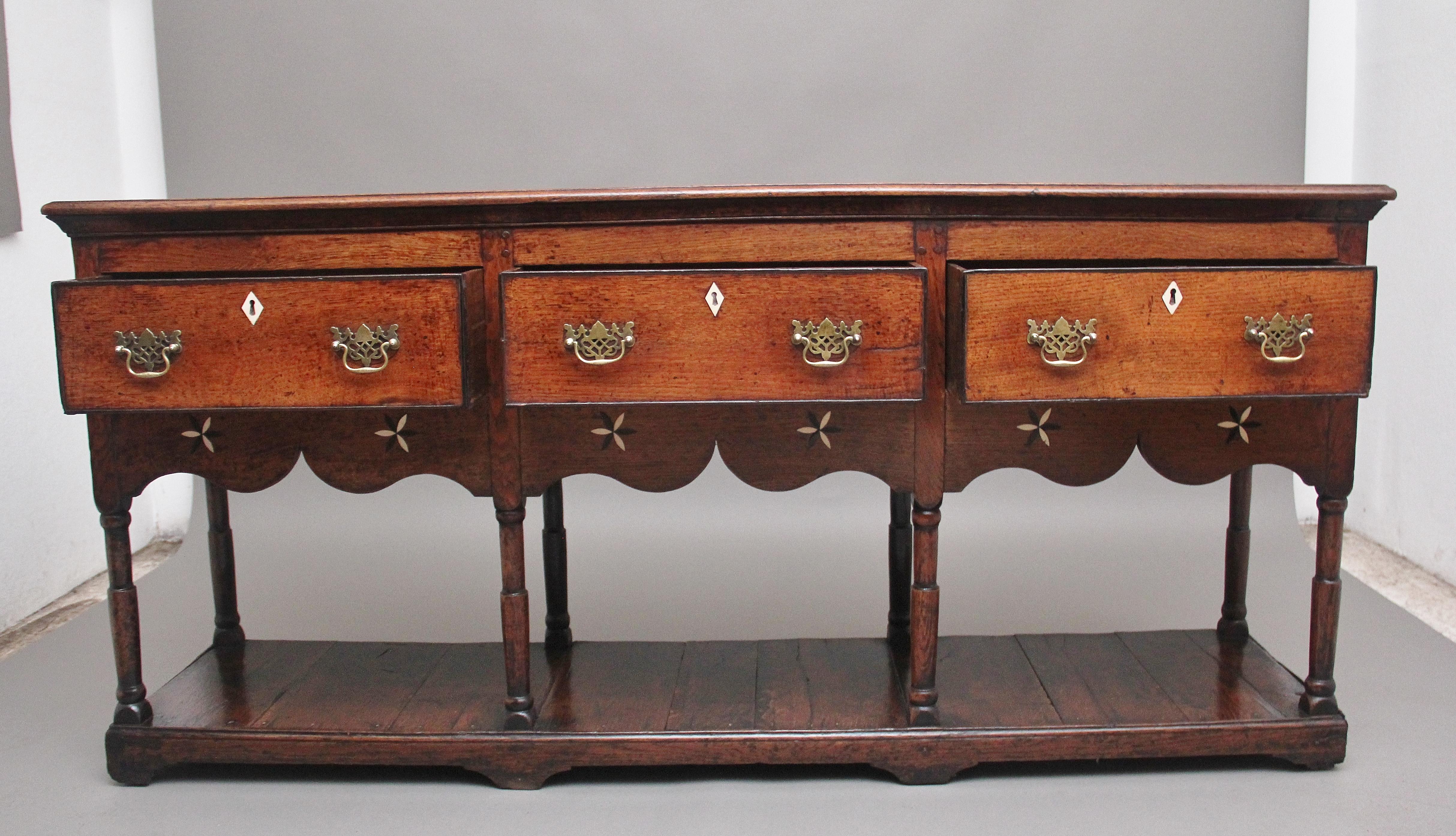 18th century oak dresser base, having a nice figured top with a moulded edge above three deep oak lined drawers with brass fret handles, shaped frieze below with decorative bone and ebony inlay shapes, turned columns supports terminating onto a