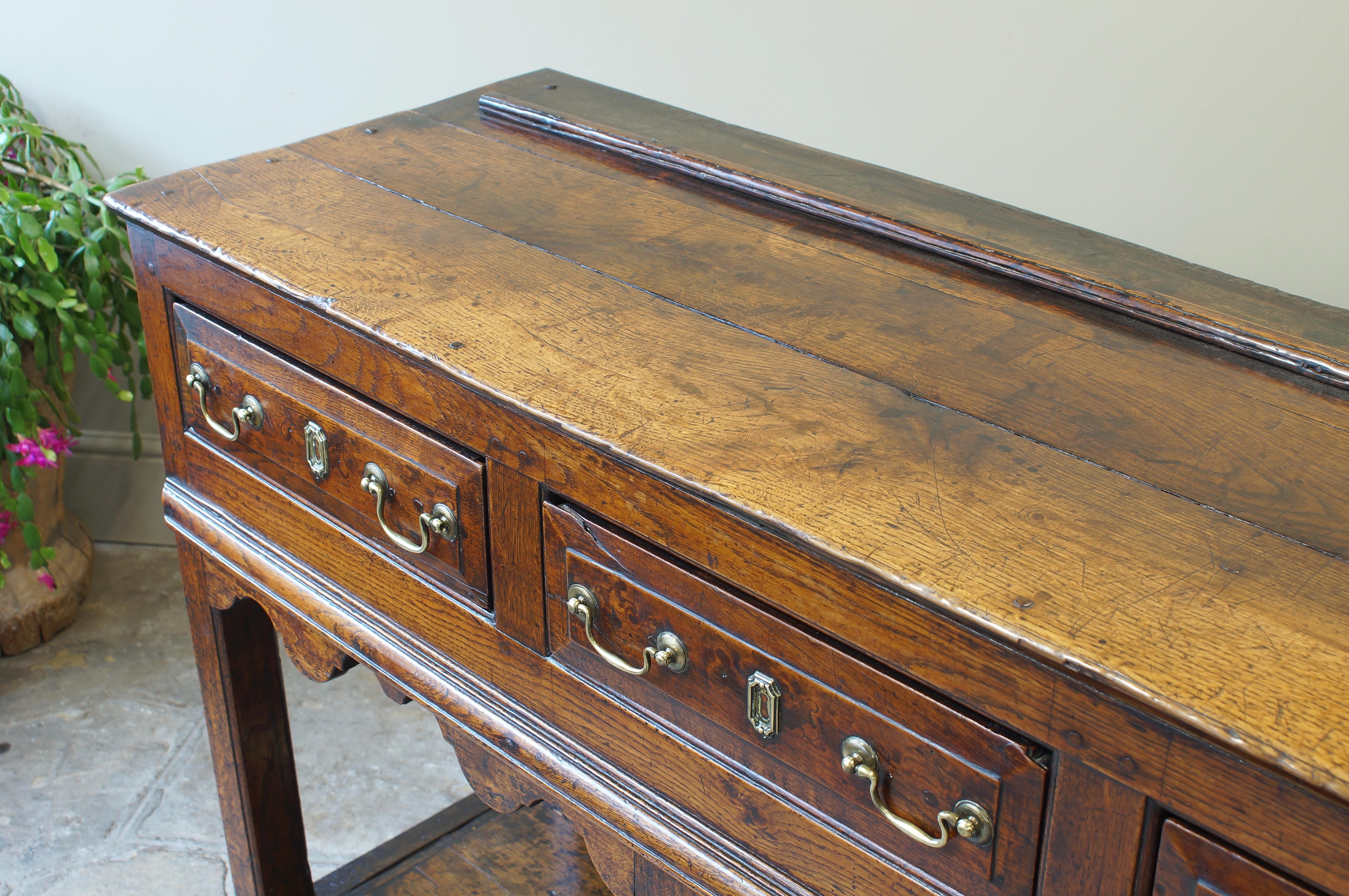 An oak four drawer dresser base, having four fielded drawers, a well shaped frieze, two central silhouette legs leading to a potboard. Having oak lined drawers and an excellent colour throughout.
With later handles and historical restoration to the