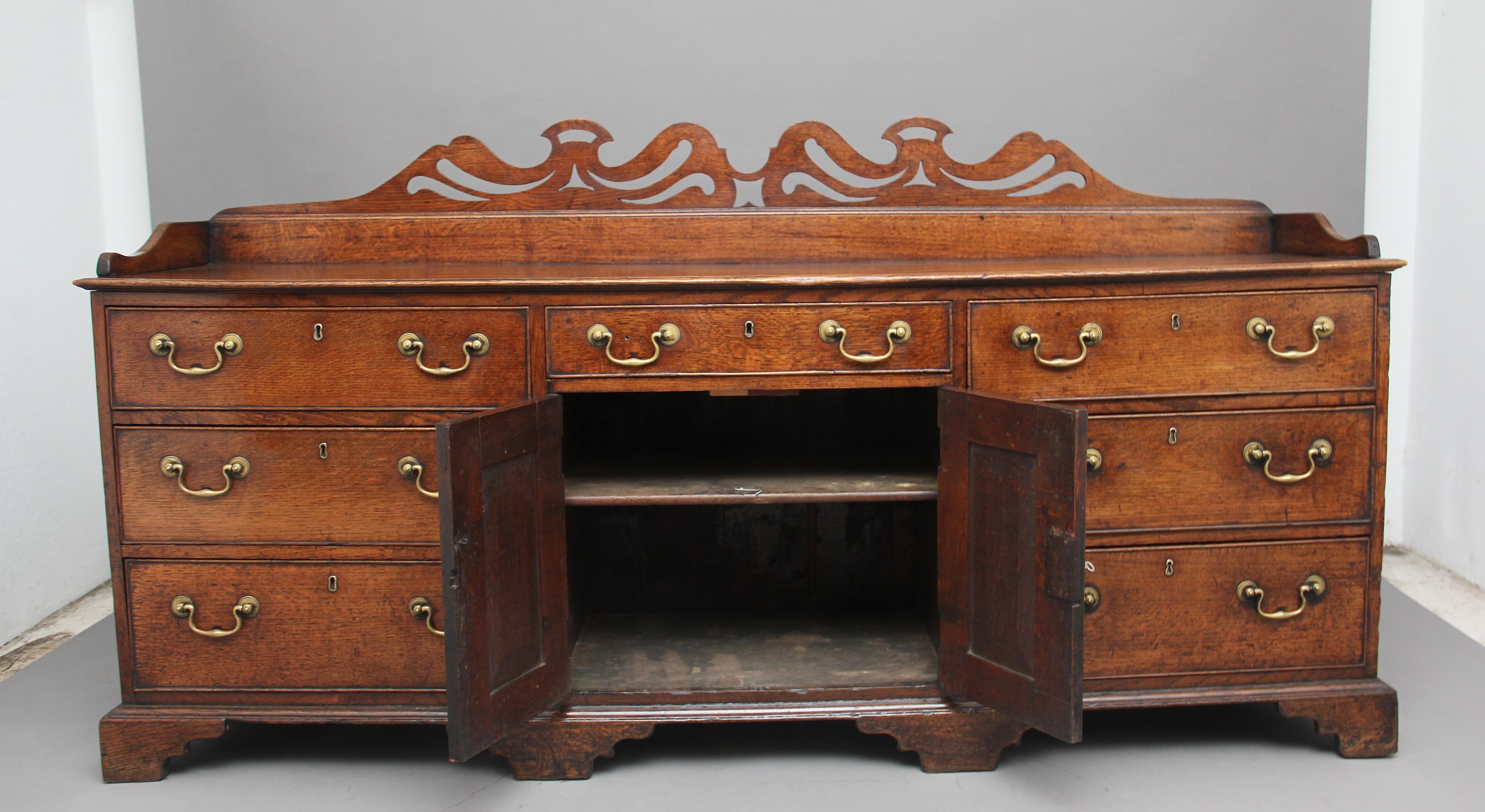 A very good quality 18th century oak dresser, the top having a three quarter gallery with a pierced frieze above a selection of seven graduated oak lined drawers with brass swan neck handles, the centre of the dresser having twin panelled cupboard