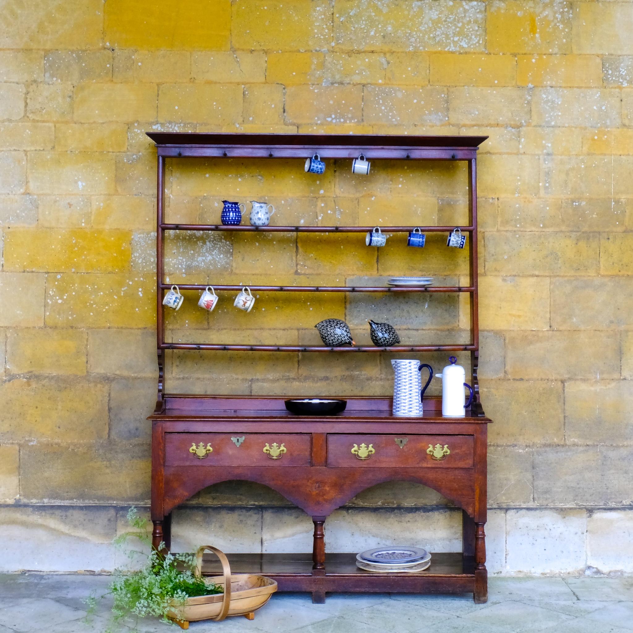 An 18th century dresser in a beautiful rich oak, with open plate shelves over a two drawer base with a twin arched apron on turned legs with a boarded lower shelf. Various hooks along the three shelves and top. Comes in two pieces for easy transport
