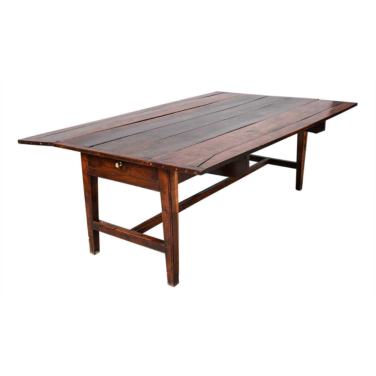 Table de campagne en chêne à feuilles tombantes, reposant sur des pieds effilés reliés entre eux par des montants en H simples. Le dessus de la planche est clivé à chaque extrémité. Le tablier est équipé d'un tiroir à chaque extrémité. Les boutons