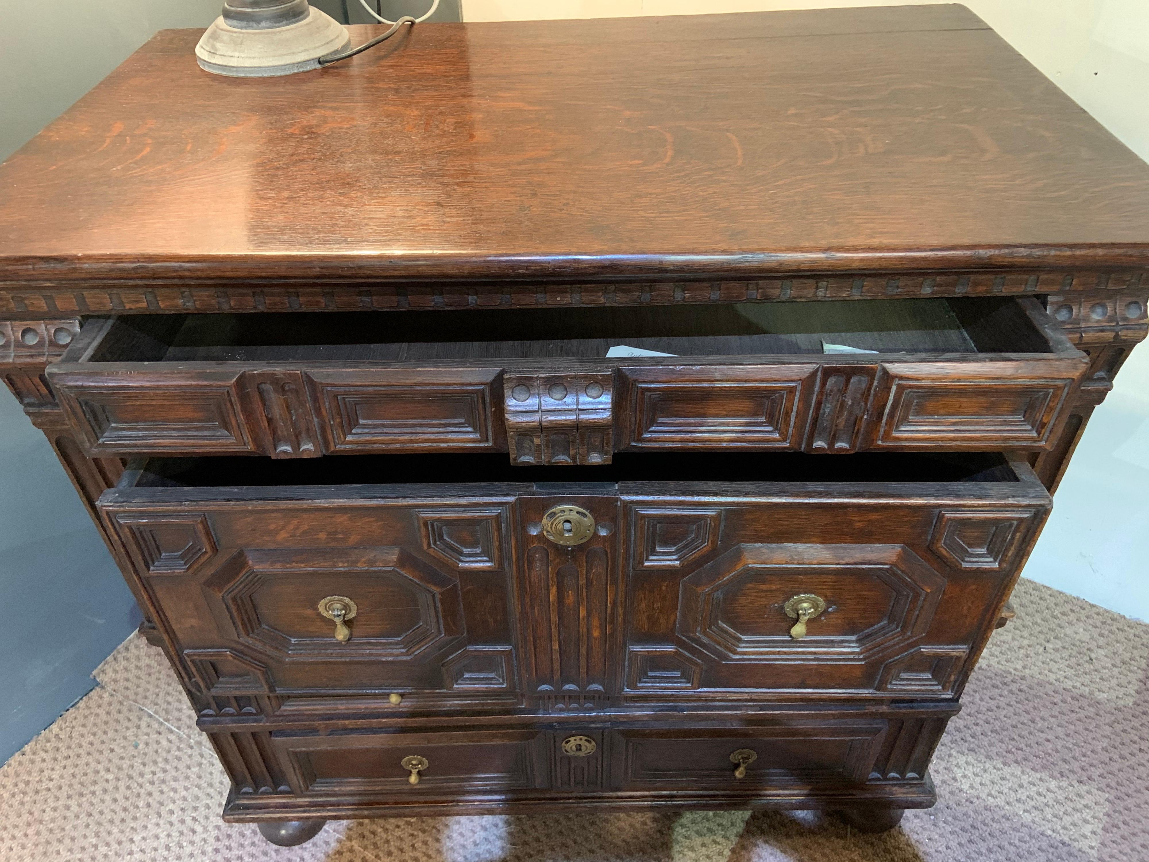18th century oak architectural geometric chest of drawers. Top hangs over four drawers of varying sizes, having geometrically moulded fronts opening on side runners. Chest of drawers stand on bunn feet. Rich color and patination. Very solid, sturdy