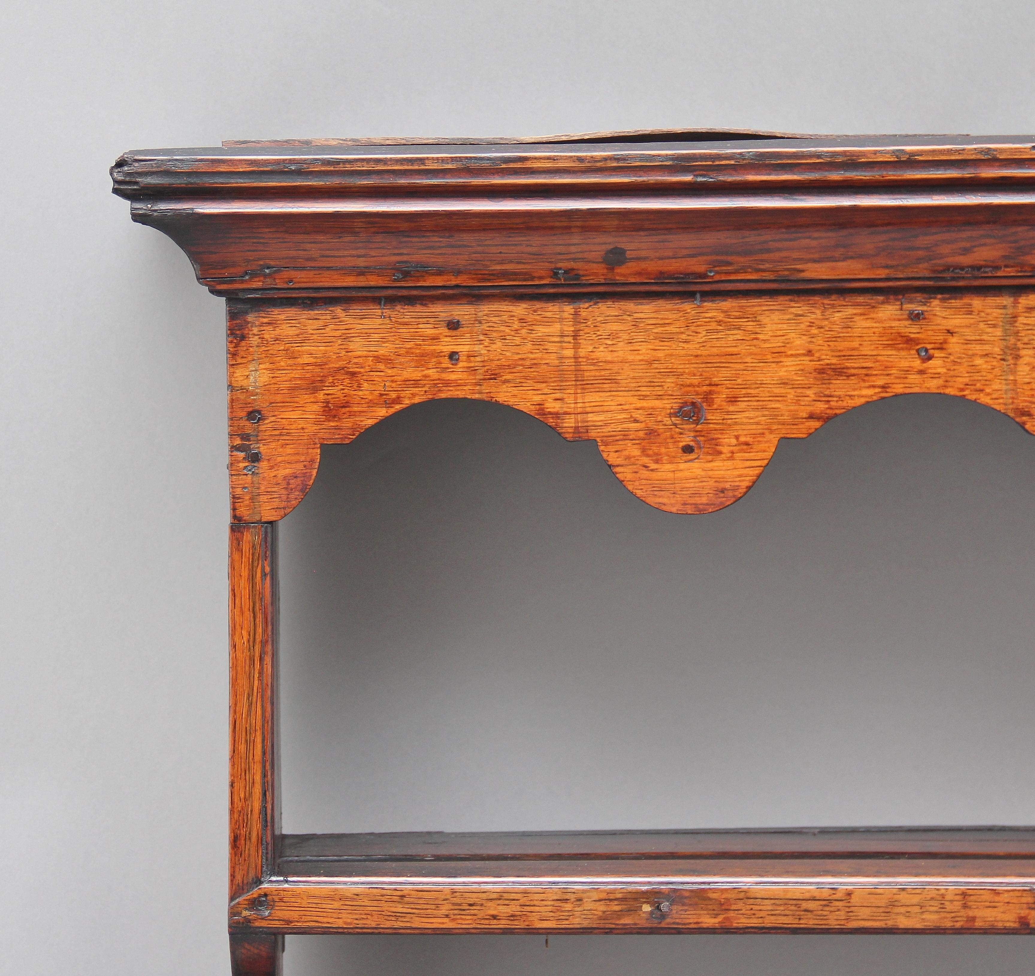 18th century oak hanging rack, the moulded cornice above a scallop-edged frieze rail, two open shelves with plate grooves and brass cup hooks, shaped end supports. Lovely color, circa 1780.