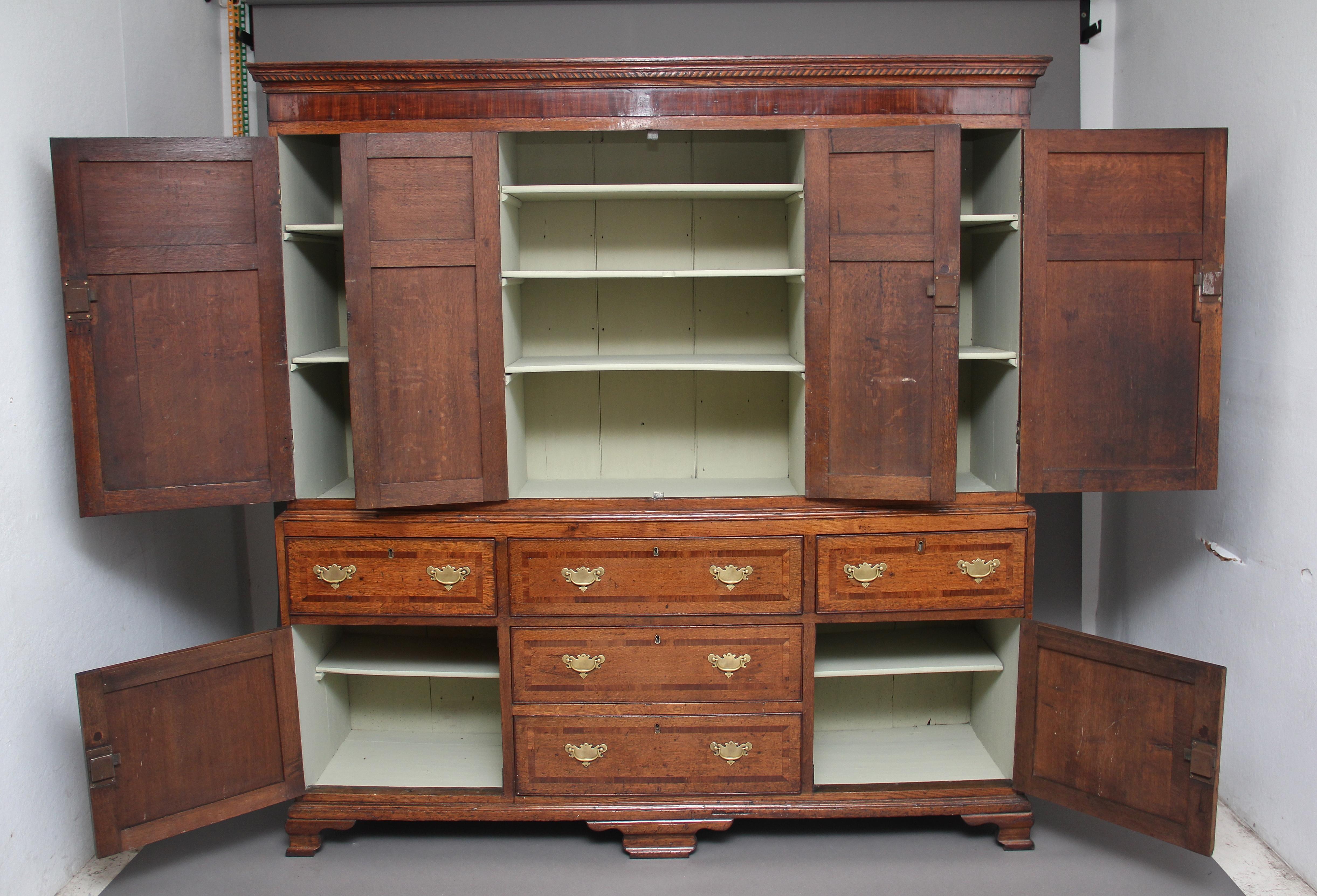 18th century oak housekeepers cupboard of good proportions, the cupboard is in two sections, the top section having a stepped moulded cornice above a four door cupboard, the door fronts having fielded panels with crossbanding, the two doors at the