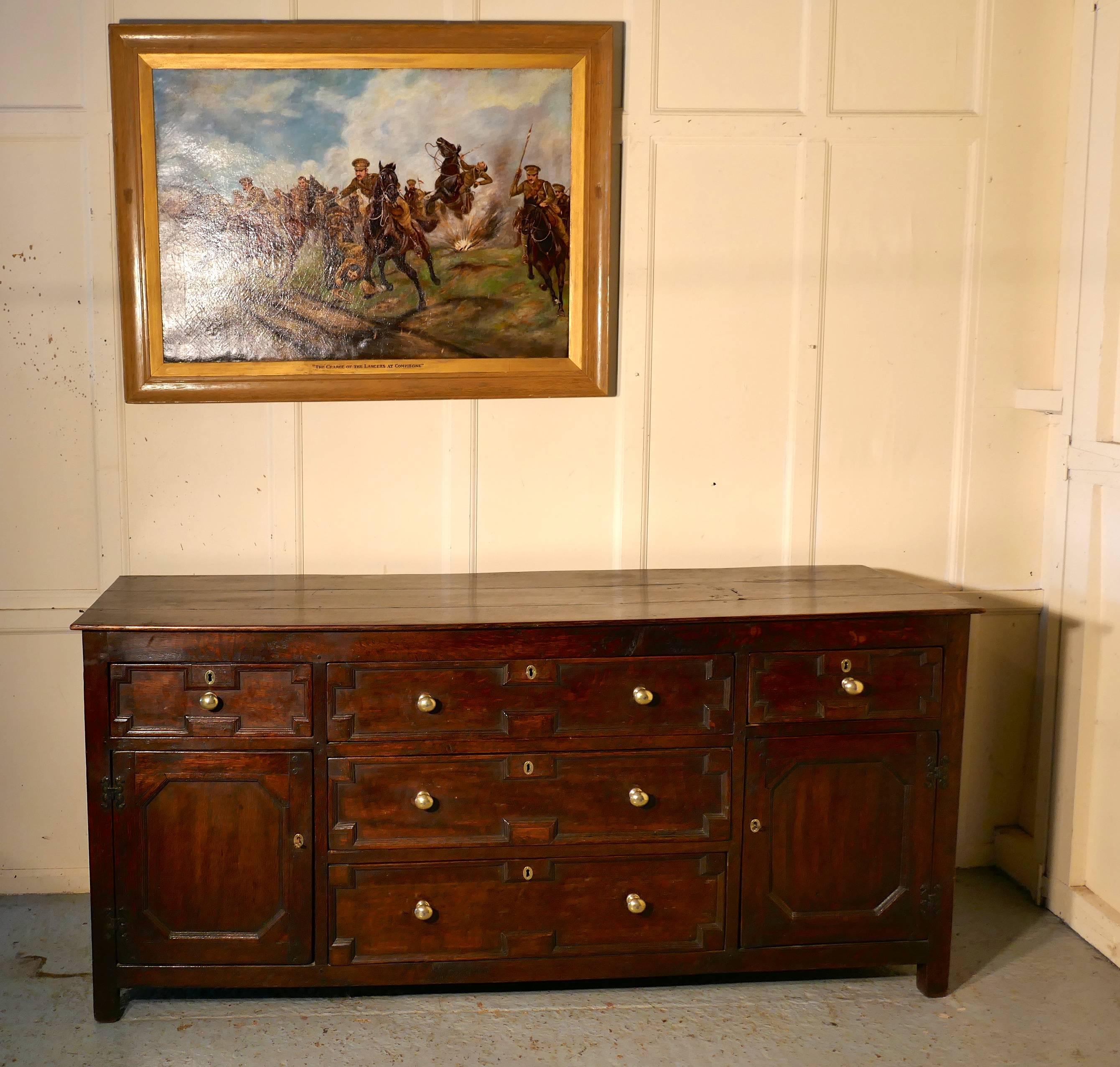 18th century oak long dresser base

This is fine looking piece, dating from the mid-18th century
The dresser has a three plank top, it has a bank of three graduated drawers in the centre, flanked on each side by a panelled cupboard door with a