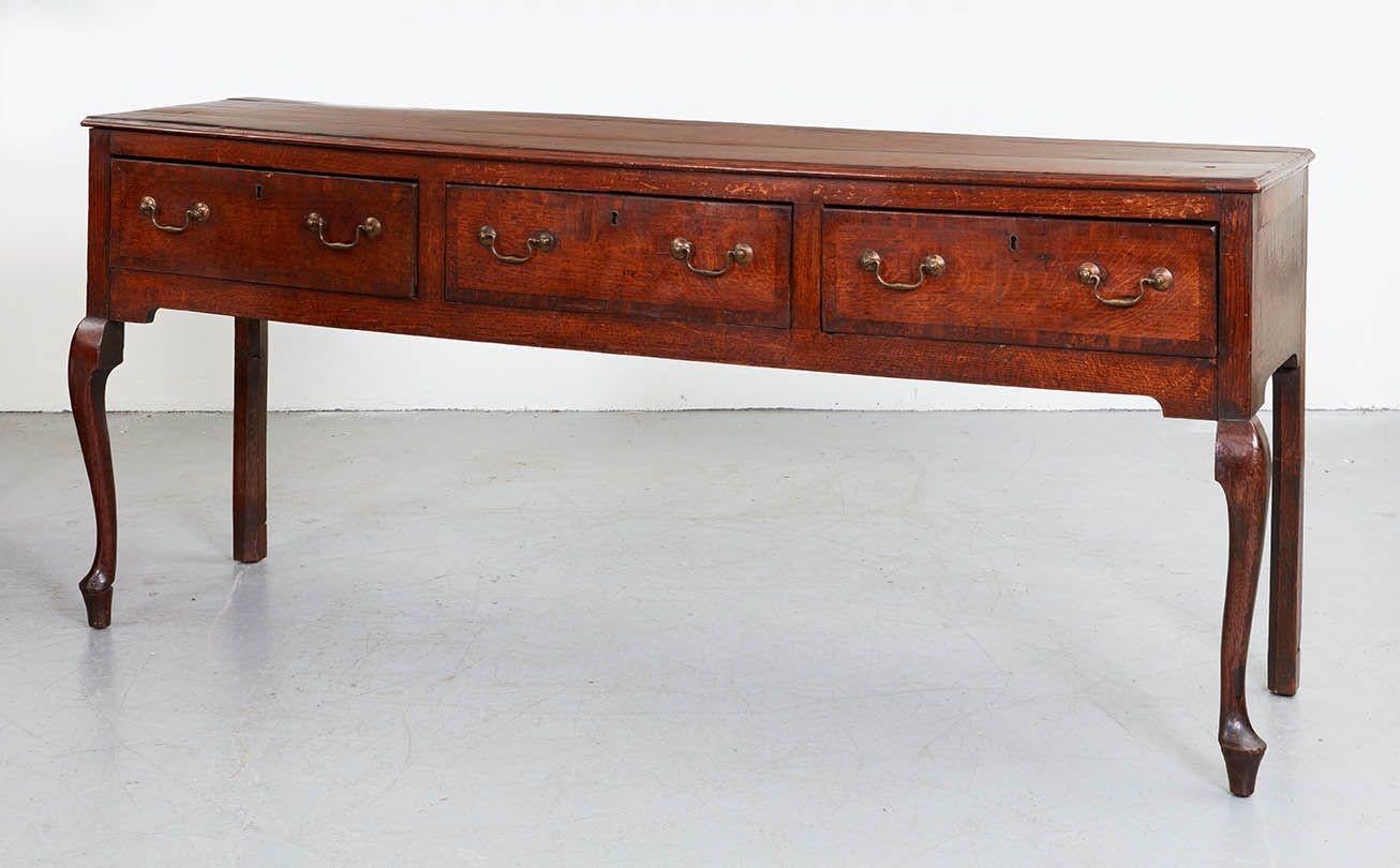 Late 18th century Shropshire or Staffordshire oak dresser base, the quarter sawn plank top with mahogany cross banding, over three drawers similarly banded, and standing on front cabriole and rear square legs, both with later (but elegant)