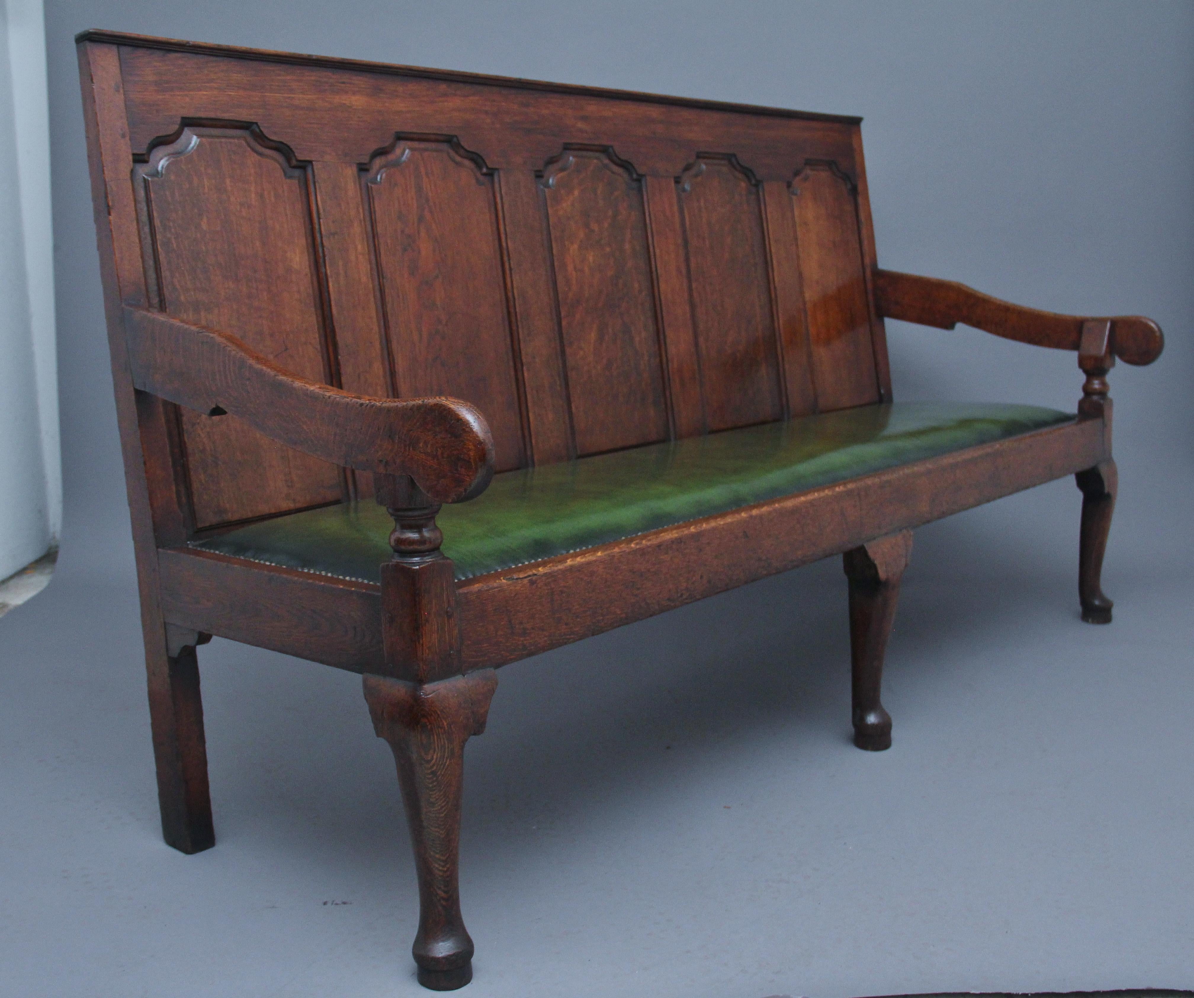 18th century oak settle / bench the high back with five fielded oak panels flanked by down swept arms on turned supports enclosing the recently upholstered green leather seat with brass stud decoration, supported on cabriole front legs and square
