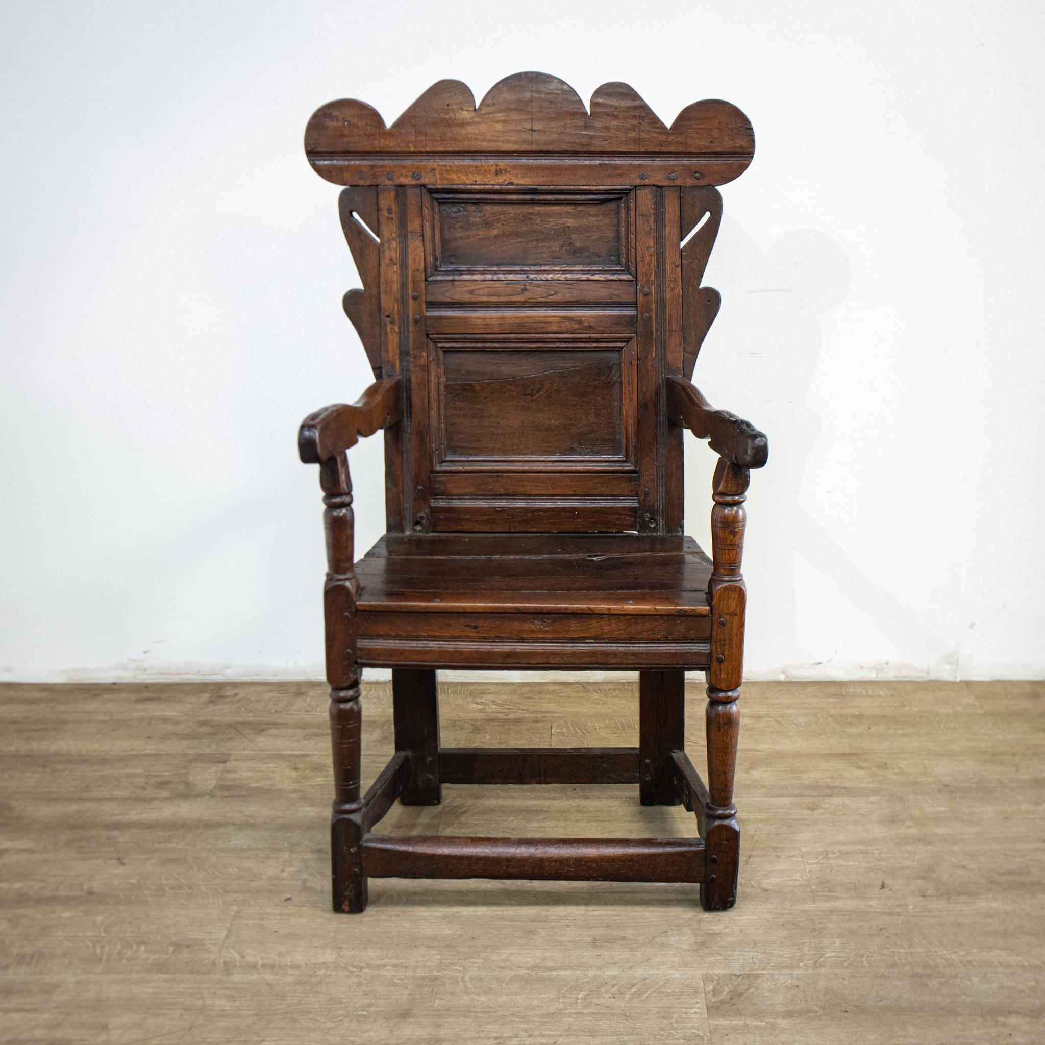 A real antique, this 18th century rustic wainscot chair has a carved shaped top rail above a panelled back, with turned front legs, square section back legs and carved arm supports. These early chairs were named after the fine grade of oak used for