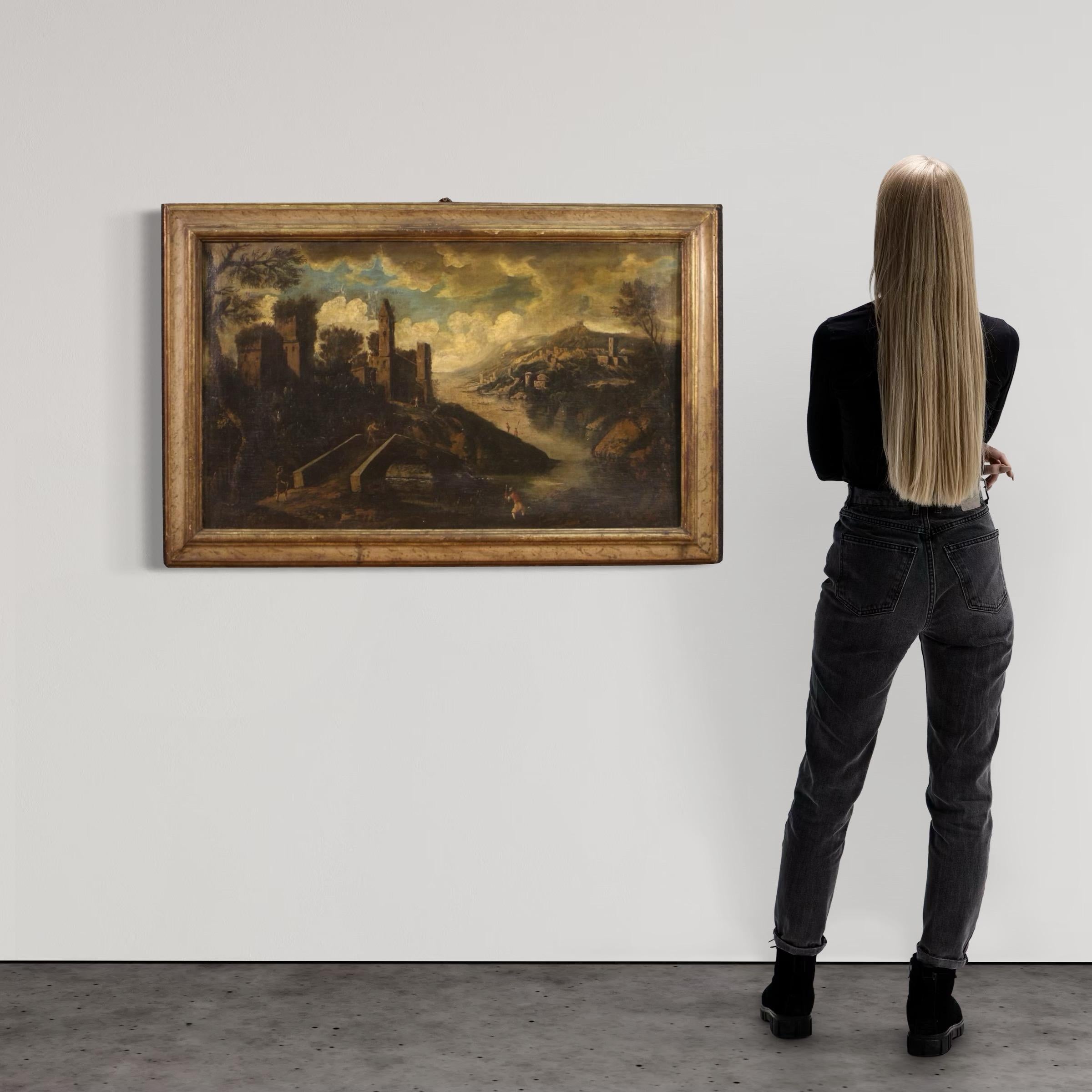 Antique Italian painting from the mid-18th century. Oil on canvas artwork depicting a landscape with characters and architecture along the river, of good pictorial quality. Finely carved, gilded and lacquered antique wooden frame of pleasant