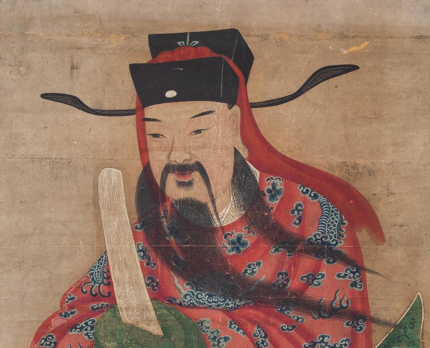 Large Chinese painting of a Chinese Lohan with flowing hair, mustache, beard and black headdress, wearing a colorful red loosely draped robe decorated with blue dragons and flowers, green lining, holding an ivory sword. There is a shield enclosing