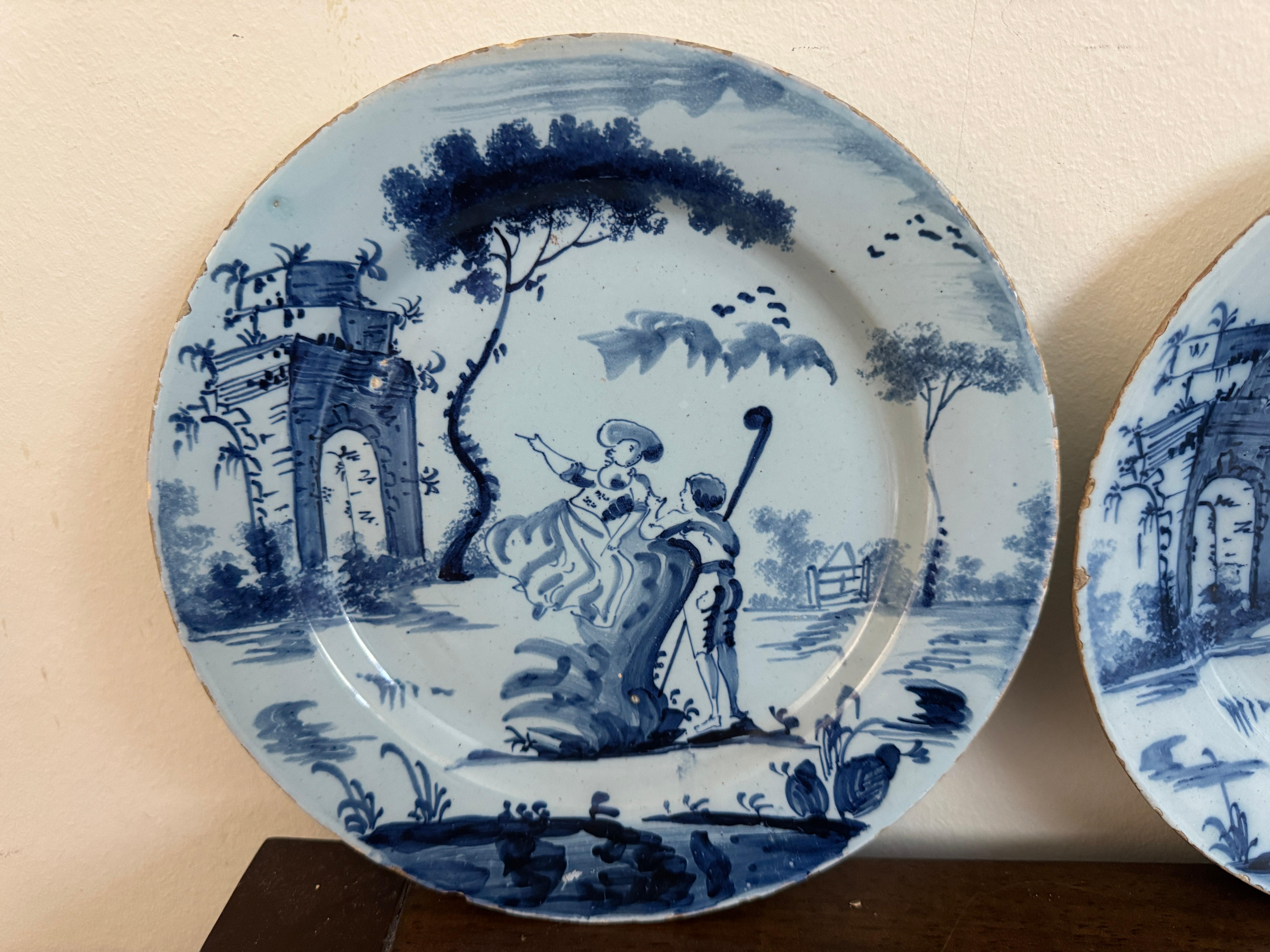 Siglo XVIII Pareja de platos ingleses de Delft azules y blancos, hacia 1770, que representan la escena de una dama en un banco señalando un arco en ruinas con un pastor con cayado a su lado. 