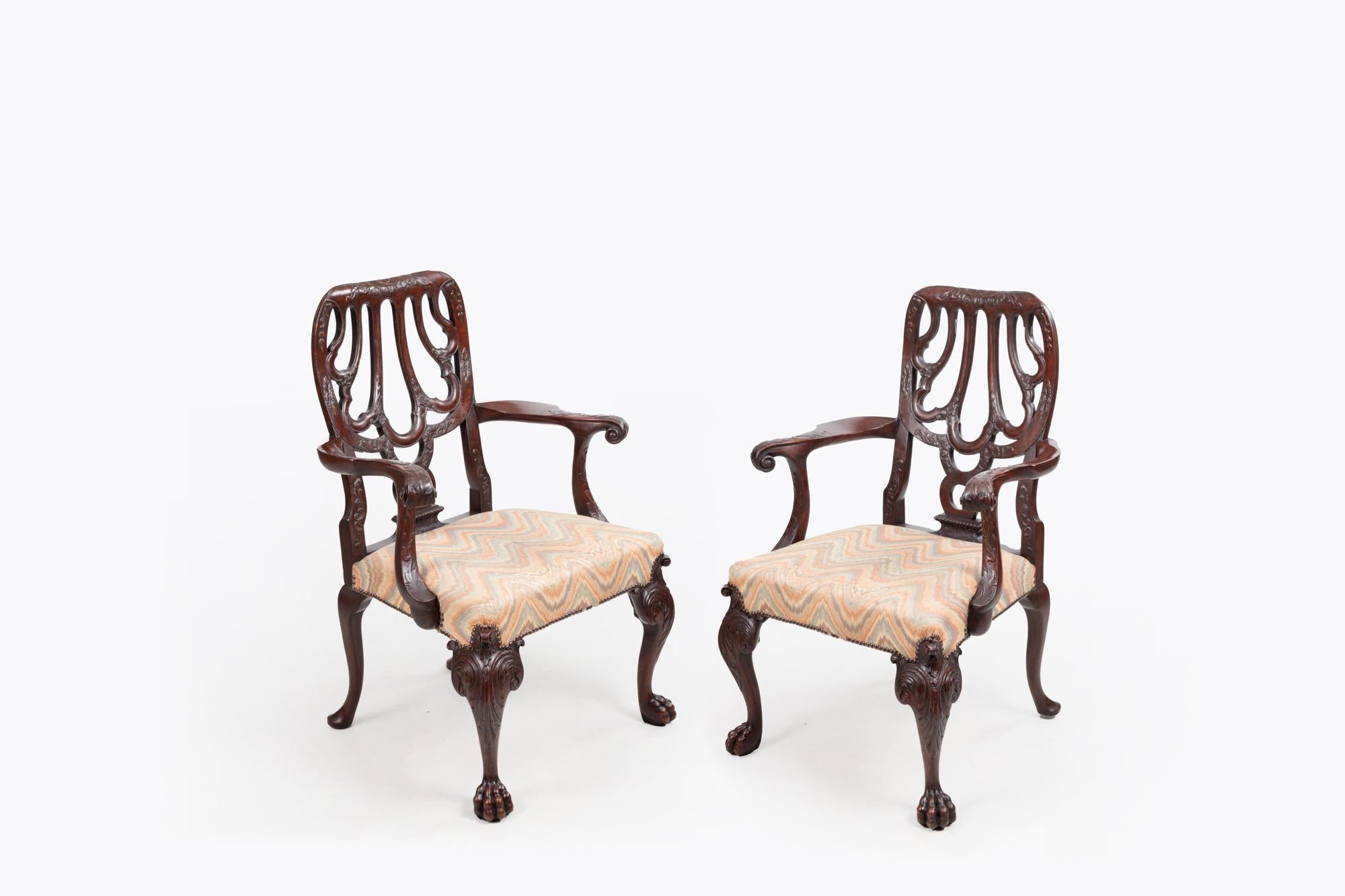 18th Century pair armchairs after Giles Grendey with pierced splat back, stylised shell motif and scrolled armrests with relief carved decoration. The upholstered seats rest above carved cabriole legs with scroll and acanthus leaf decoration