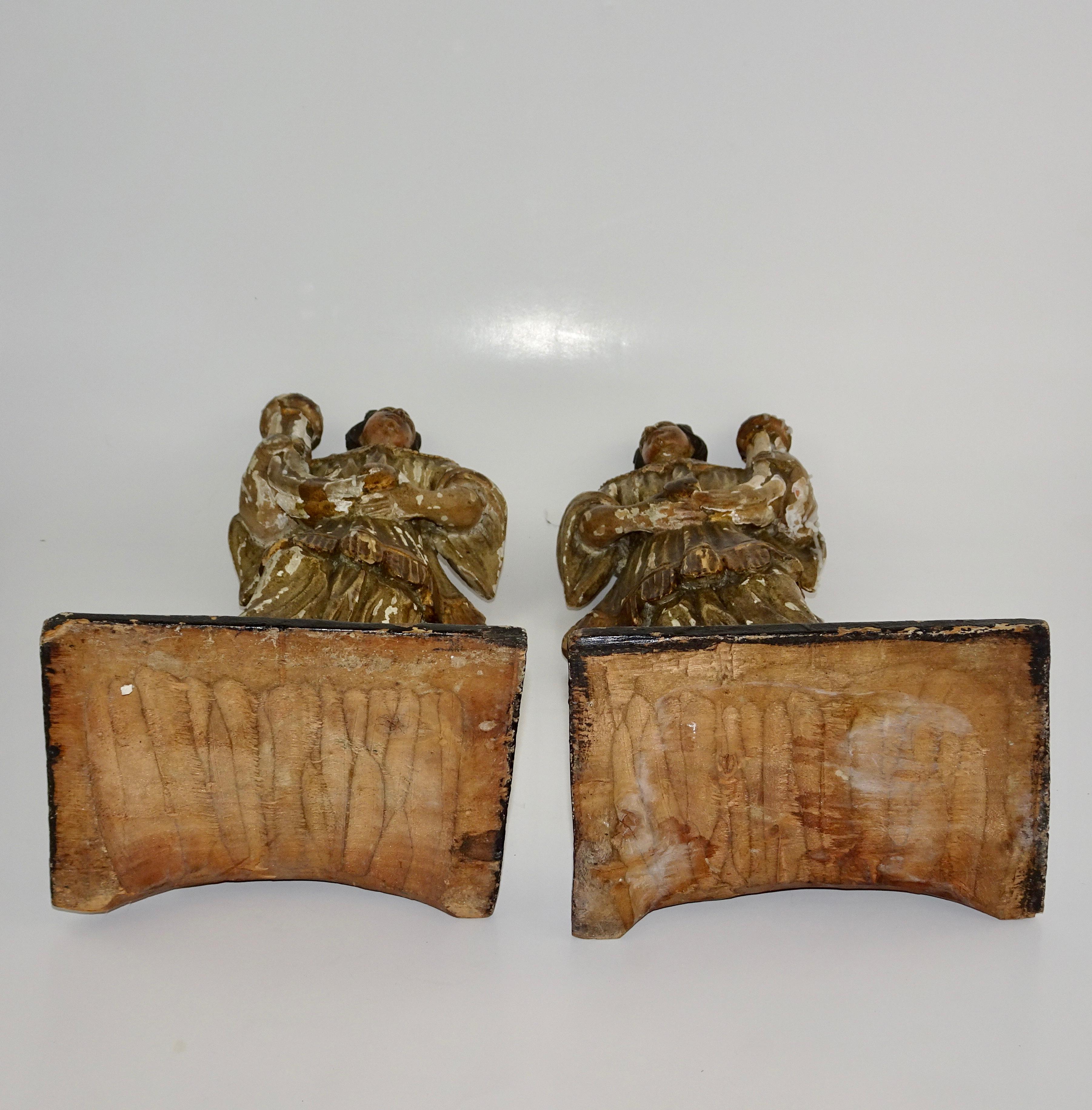 Pair of 18th century wood carved Italian figures of angels holding candleholders. The figures stand on a square base and one is holding to the left and one is holding to the right. They are painted and gilt.
