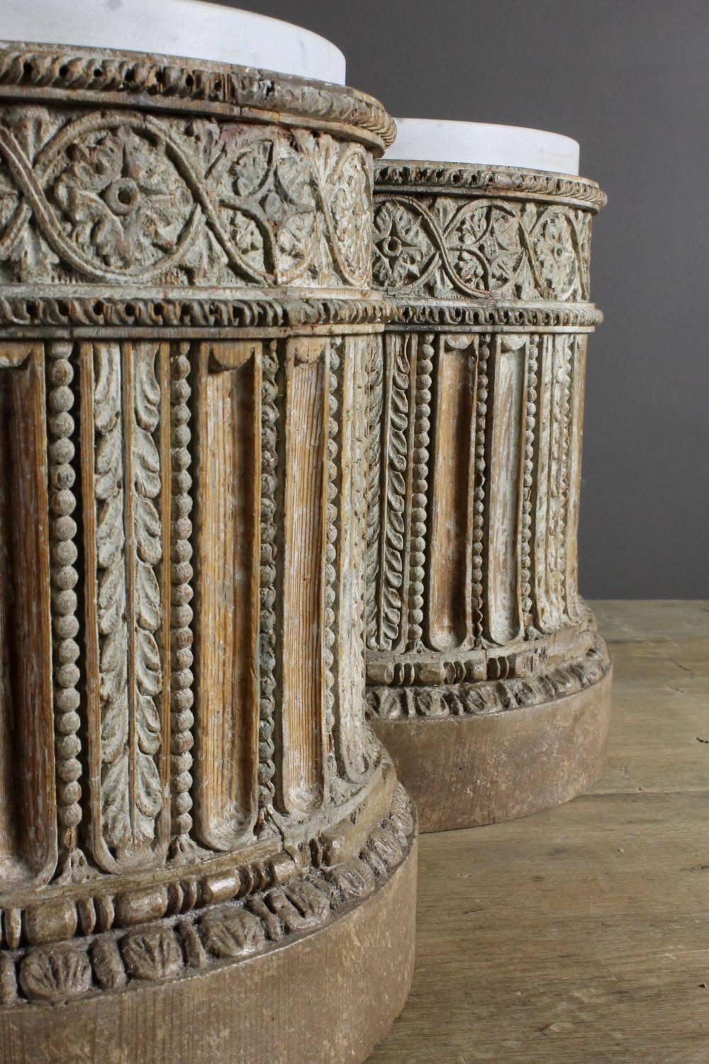 A pair of intricately carved 18th century English pine pedestal bases with traces of original gesso and original inset carrara marble tops. Circa 1780. Originally, these pedestals were covered in gilt and, at some point, that decoration has been