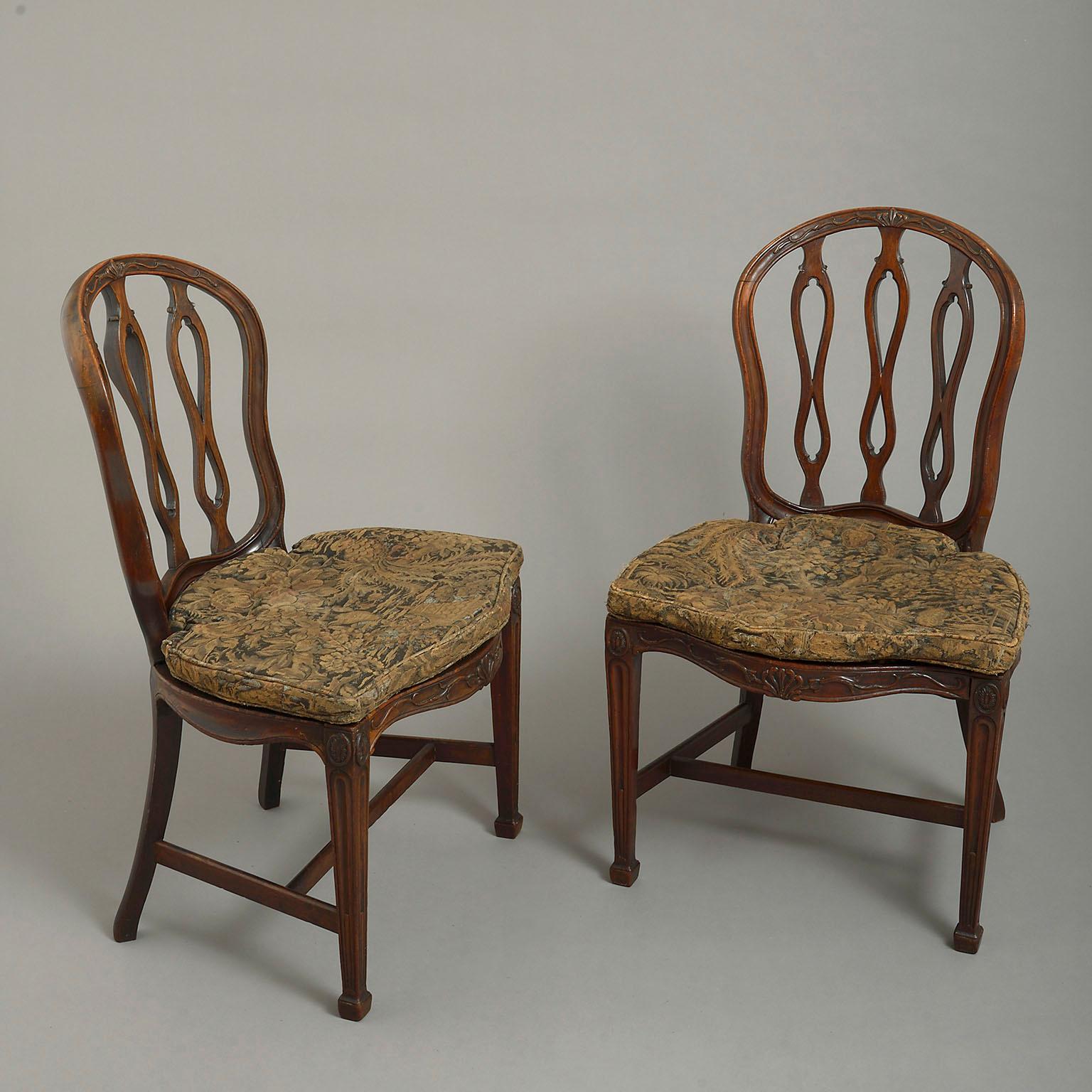A pair of 18th century George III mahogany chairs in the manner of James Wyatt, the cartouche-shaped backs each with three pierced interlaced splats, the caned serpentine-fronted seats with conforming squabs and raised on square tapering legs.
