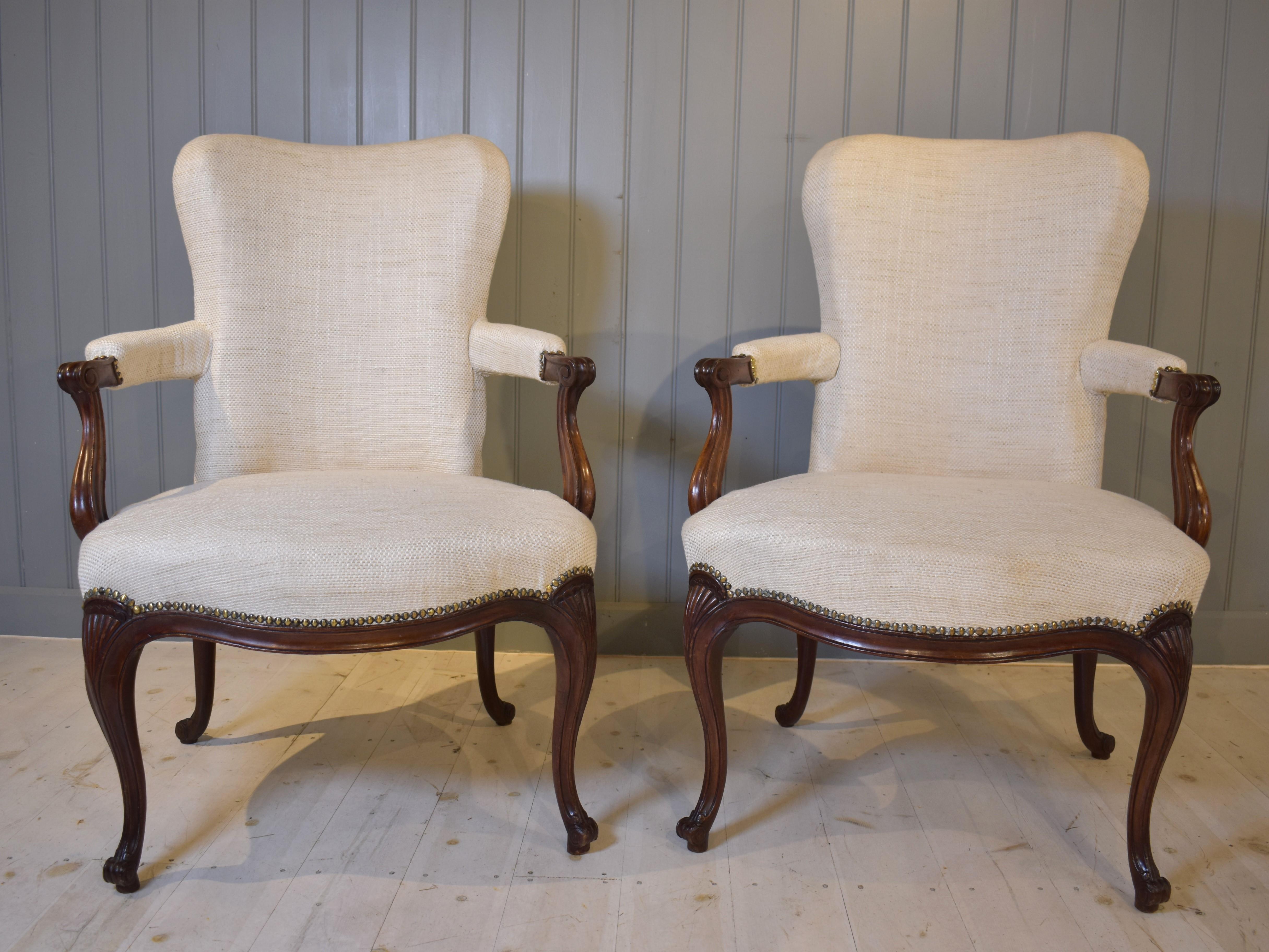 
Fine pair of 18th century mahogany open armchairs in the French Hepplewhite style. A style  defined by the beautiful scrolling arm  and typical cabriole legs with shell carving on the knees. Although French in design, these chairs are