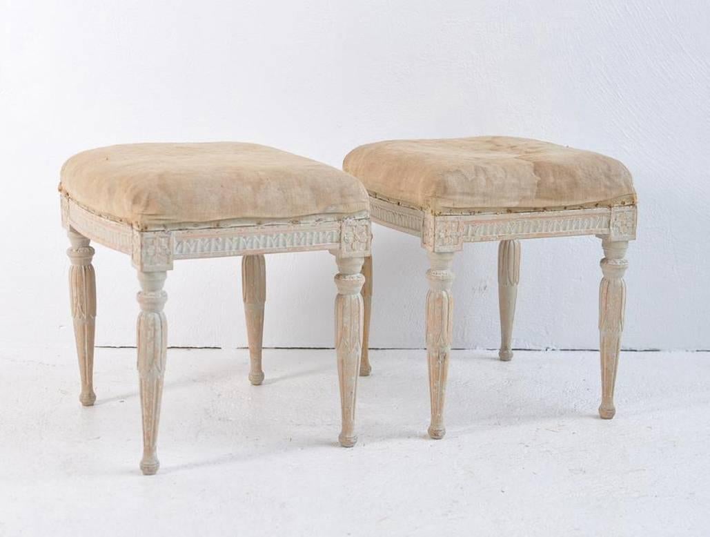 A pair of Swedish Gustavian stools by Erik Holmberg, chair maker in Stockholm between 1791-1796. Signed EHB. This charming pair has been hand-scraped to reveal the original paint. Carved egg and dart detail around the seat frame with carved rosettes