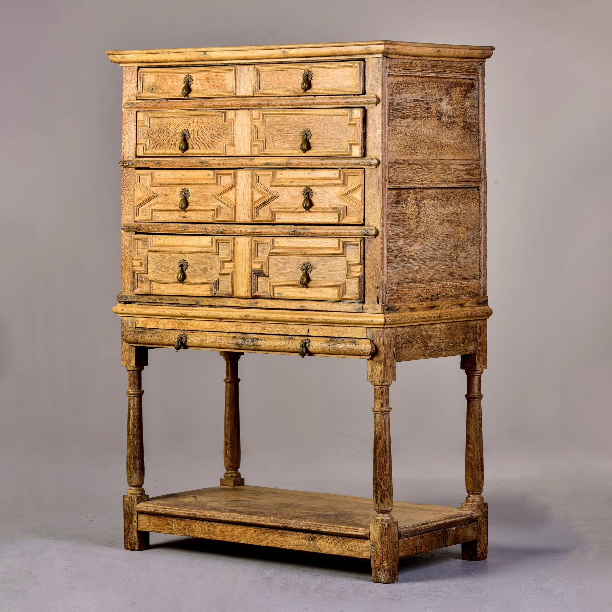 Circa 1780s English four drawer chest on stand in pale oak with original brass drop pulls in form of flower bud. Lower pull out shelf, carved details on drawer fronts. Some evidence of former/inactive wormholes and some drawer bottoms have