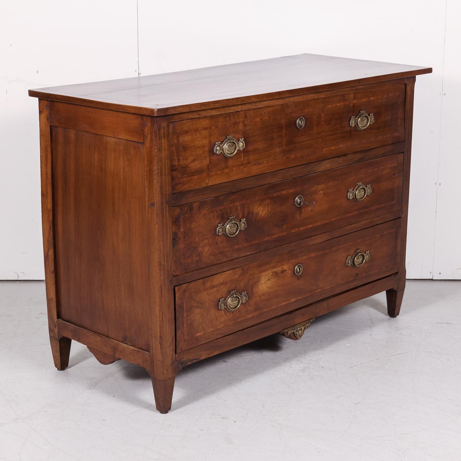 A fine 18th century French period Louis XVI commode in neoclassical form handcrafted of walnut with fruitwood parquetry by skilled artisans from Lyon, circa 1770s. Having a rectangular top sitting above three drawers adorned with original bronze
