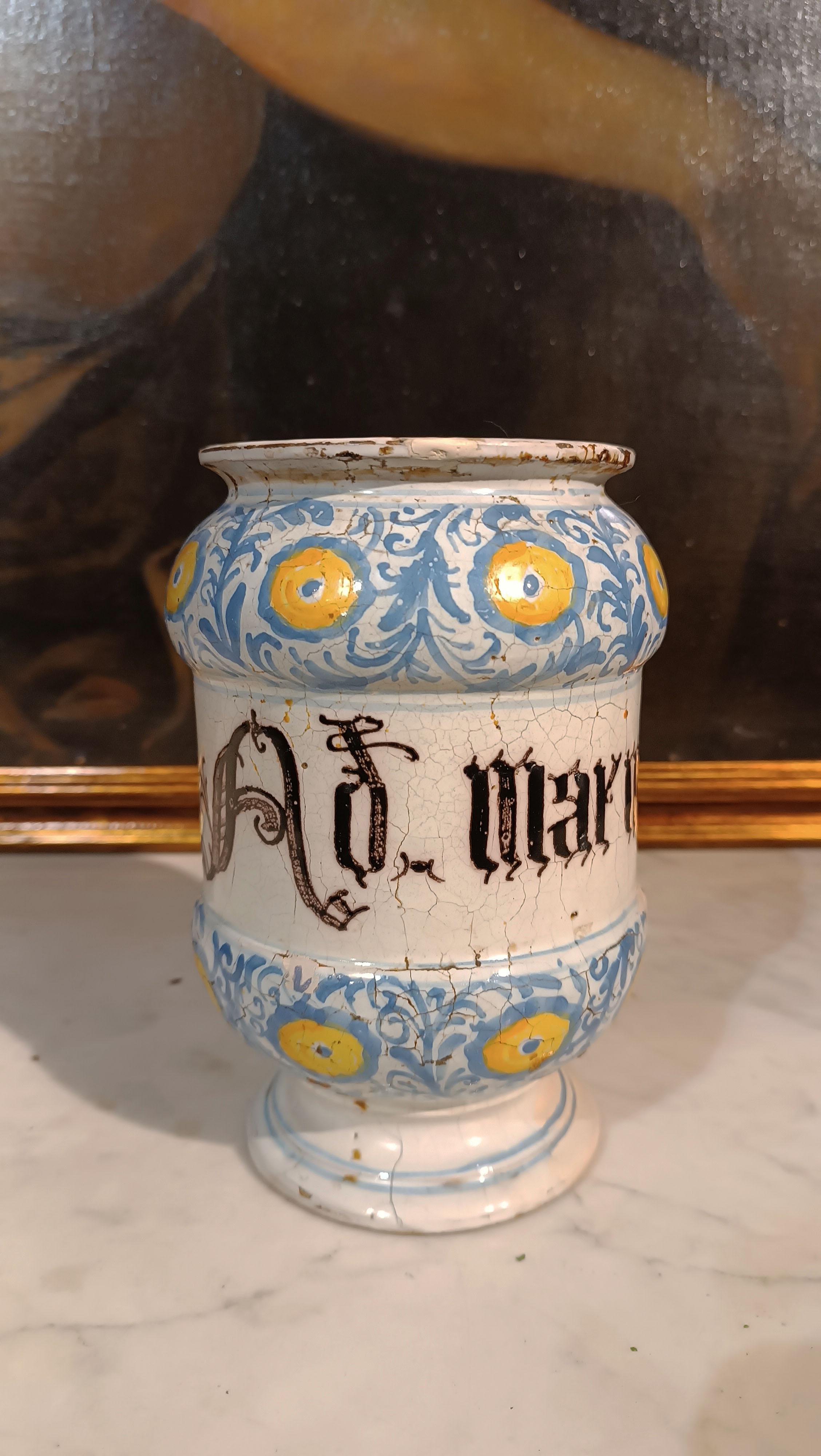 Pharmacy albarello made of majolica, with a particular spool shape. The predominant glaze of the ceramic is white, on which there are decorations in blue and yellow. These decorations mainly consist of phytomorphic motifs, depicting stylized