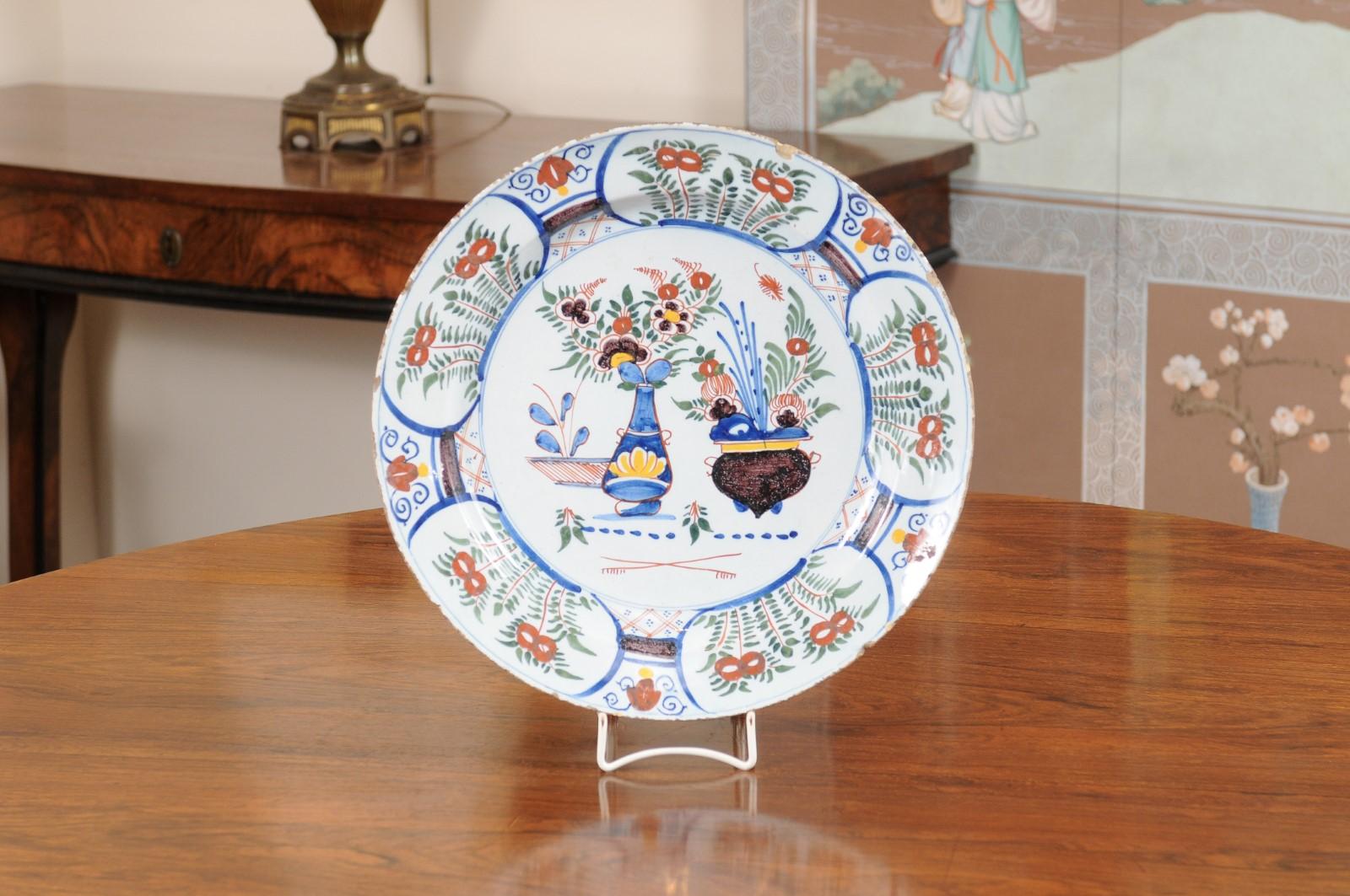 A large 18th Century Polychrome Painted Faience Charger with floral and pottery scene in the center with accents of red, green, blue and yellow.