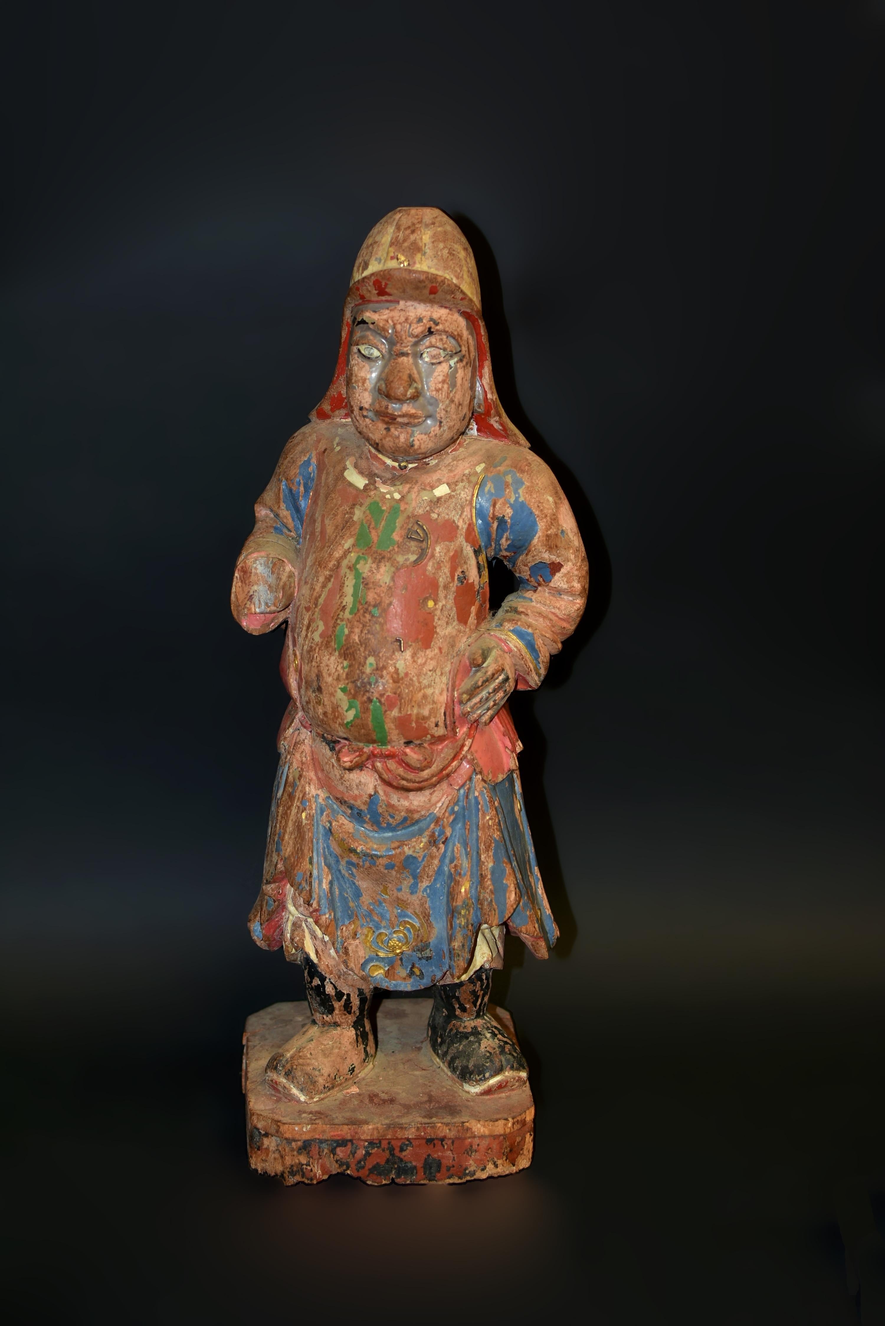A fantastic Ming dynasty polychrome wood statue of a Mongo warrior, standing firm and commanding, with large, alert, bulging eyes, a broad nose and mouth—facial features of the northern Chinese tribes. He wears a long, draped hat extending to the