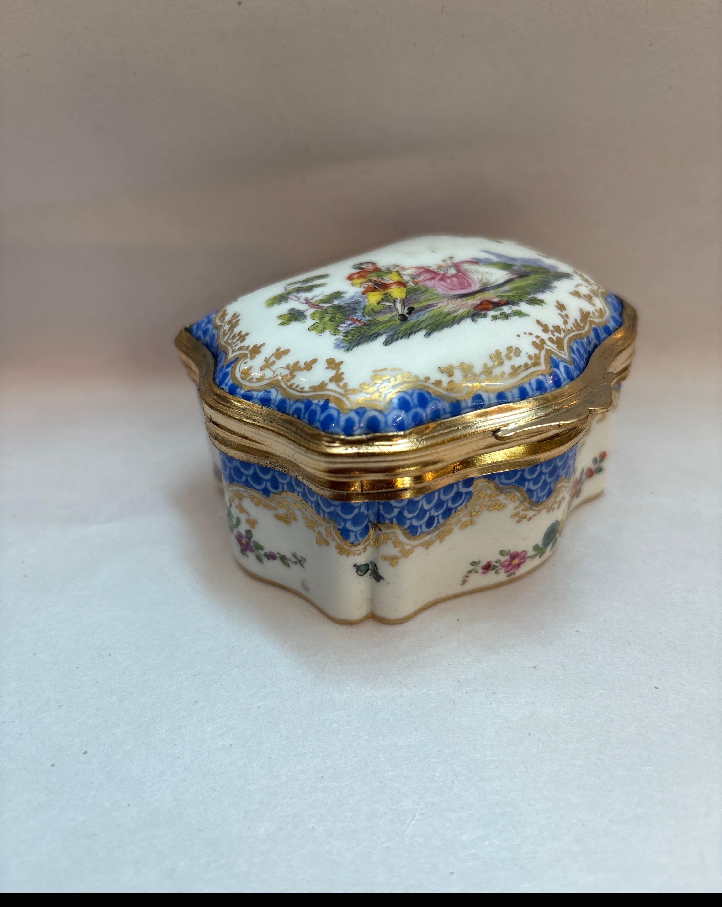An 18th century porcelain snuff or trinket posx, hand painted with a gilt bronze rim and hinge.  Made in Germany by Hochst porcelain with a gold pinwheel hallmark dating this to 1740's.  The top with a courting couple scene with floral and gilt