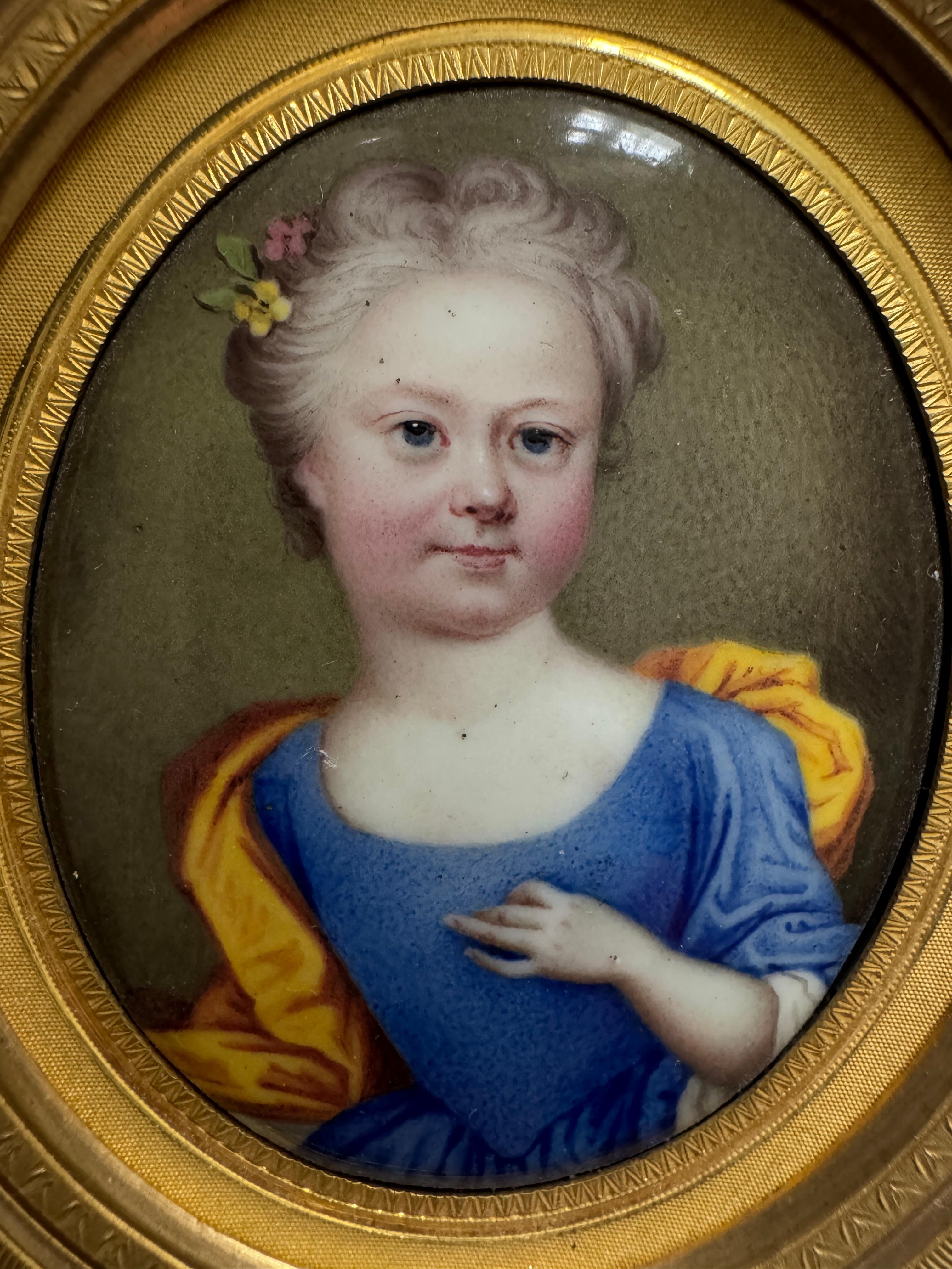 18th Century Portrait Miniature of a Child, in the style of Christian Friedrich Zincke, half length, her hair adorned with flowers and wearing a blue dress with a yellow cape enamel on copper. Oval 6cm. In a pressed gilt metal frame. circa